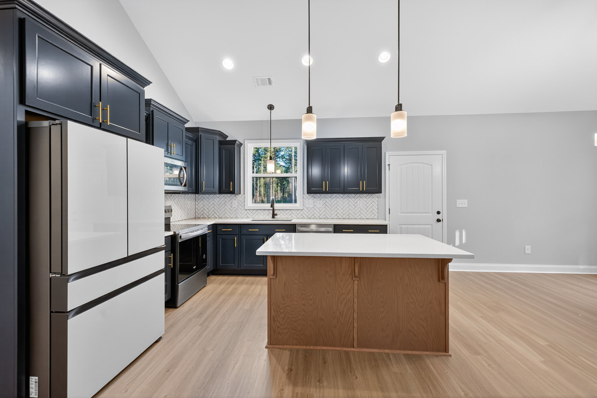 Kitchen with white refrigerator, white island, black oven with open door, white countertops, ceiling light fixture, and cabinetry.