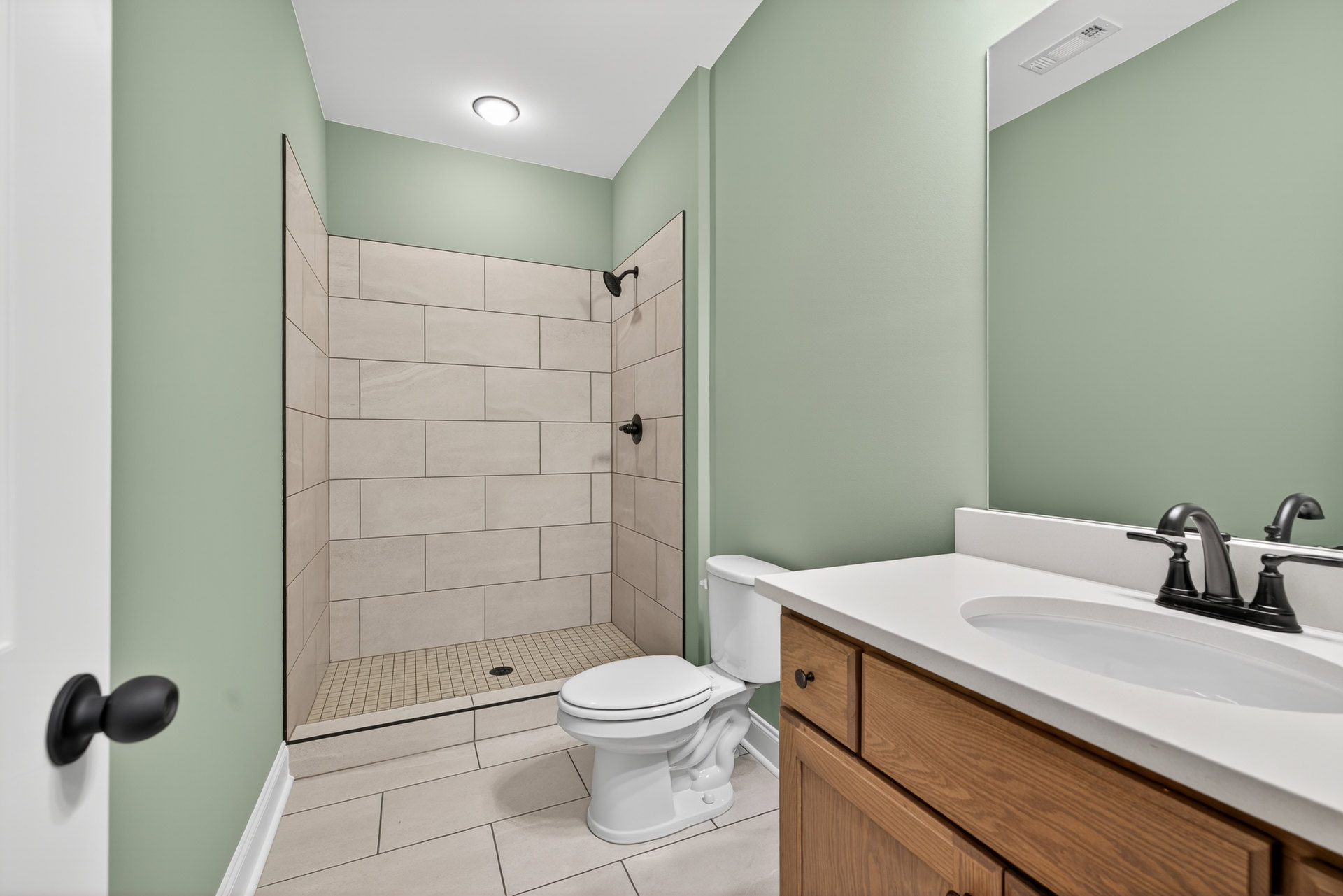 Modern bathroom featuring a glass-enclosed shower, white toilet, rectangular sink with black faucet, light gray tile walls, and a black doorknob on a white door