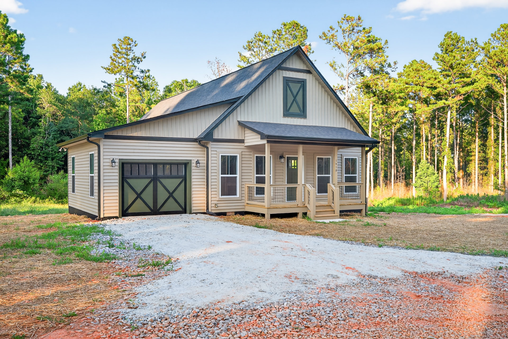 Two-story home with gray siding, white trim, attached garage, concrete driveway, front porch, and mature trees in landscaped yard