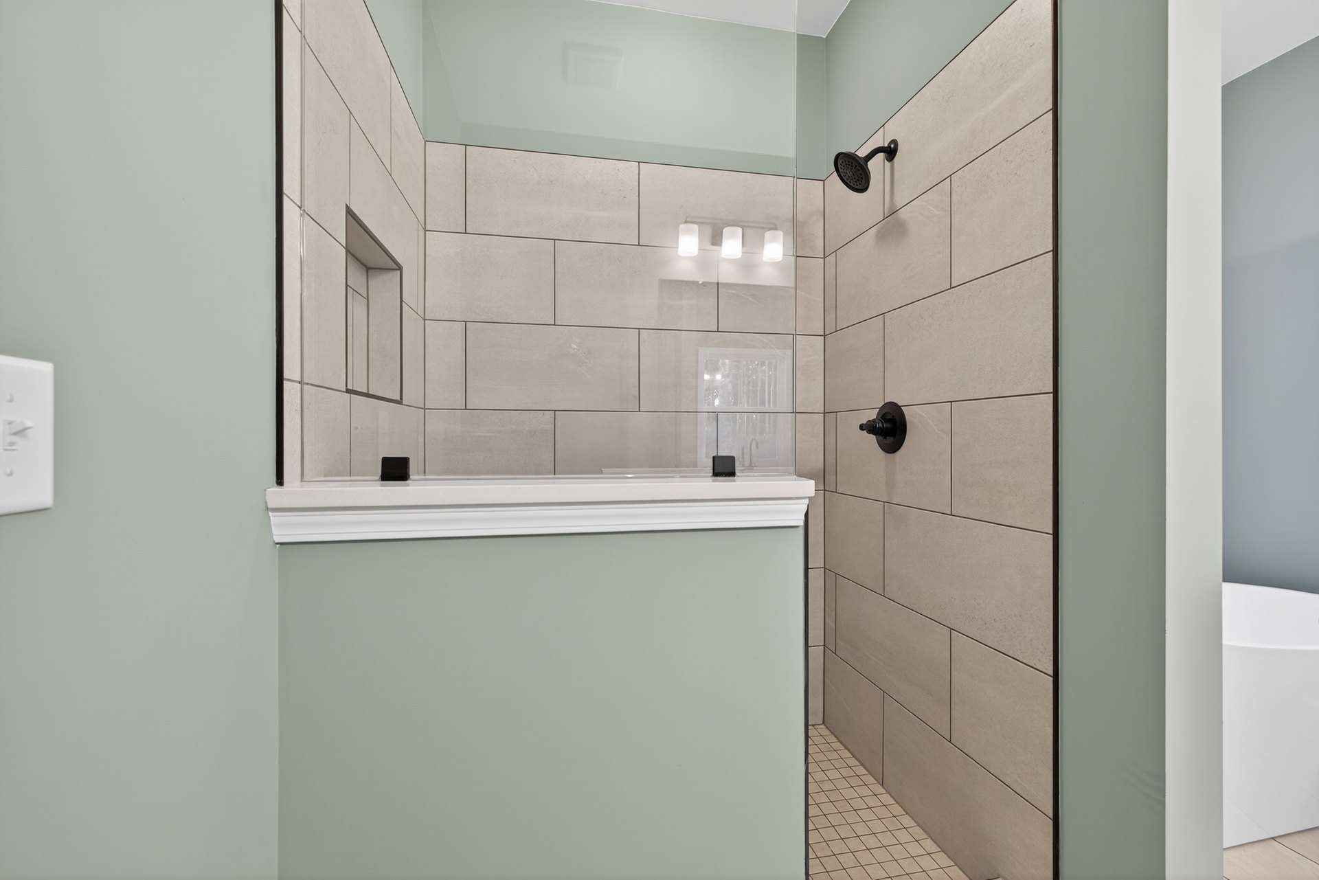 Glass shower enclosure with black hardware, white tile walls, black-trimmed board, close-up of white sink and faucet, shower head with black handle