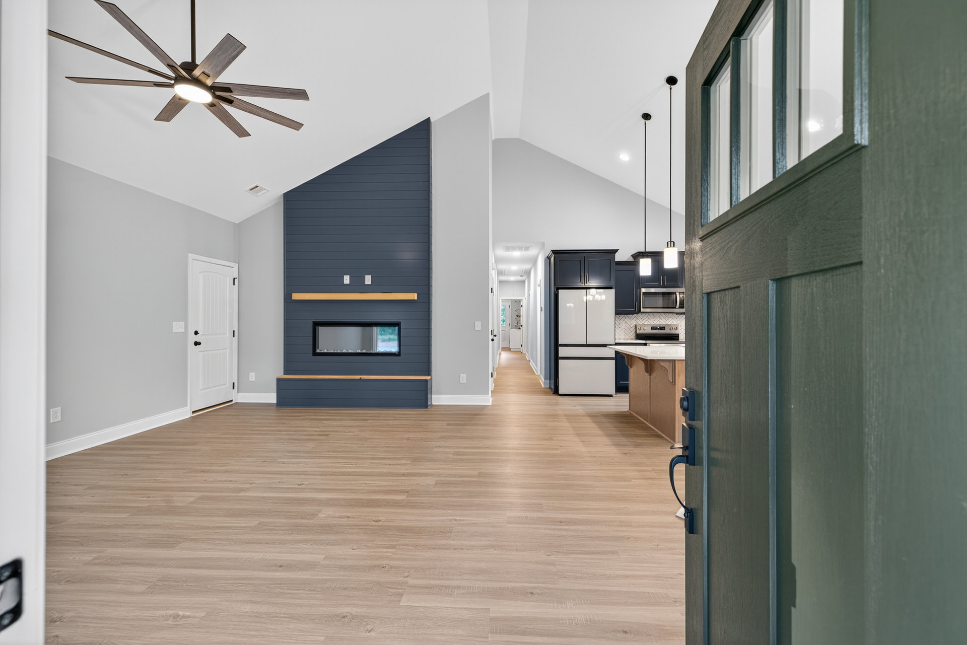 Open-concept room featuring wood flooring, white cabinetry, a ceiling fan with light, white refrigerator with black trim, fireplace beneath wall-mounted TV, close-up views of a