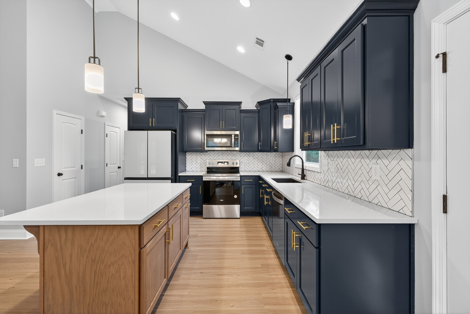 Dark blue kitchen cabinets with gold handles, white countertops, central island, stainless steel stove with glass door, built-in microwave, modern pendant light, light wood