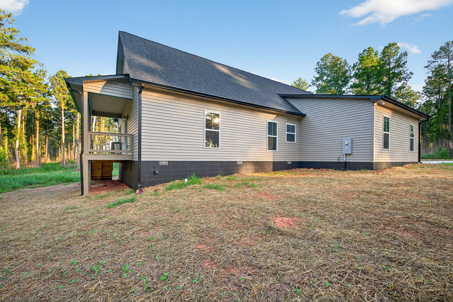 Two-story house with white-framed windows, covered porch with railing, brick foundation, green lawn, mature trees, and cloudy sky