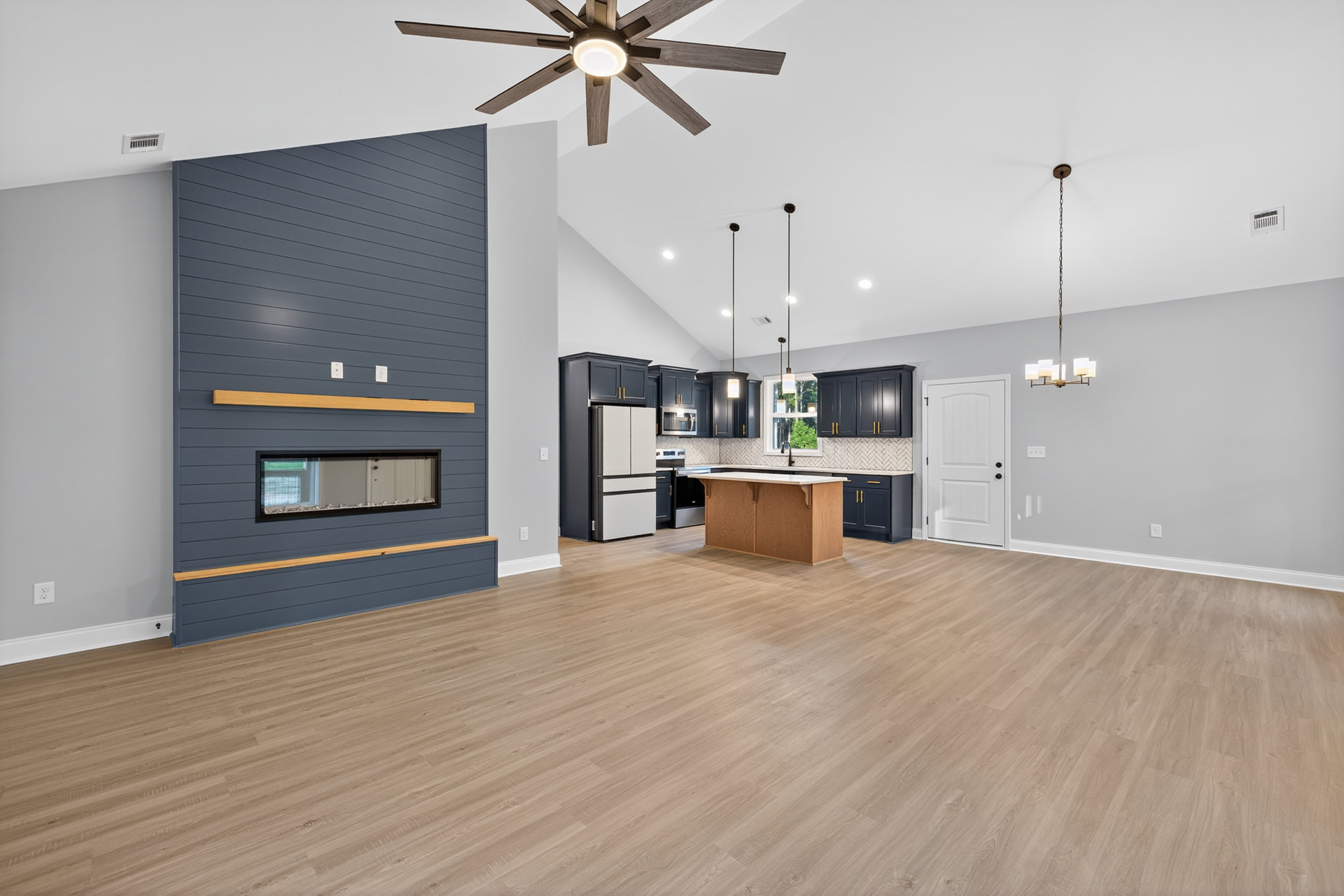 Spacious kitchen with wood flooring, central island featuring a wooden and white countertop, white cabinetry, ceiling fan with light, and fireplace along one wall