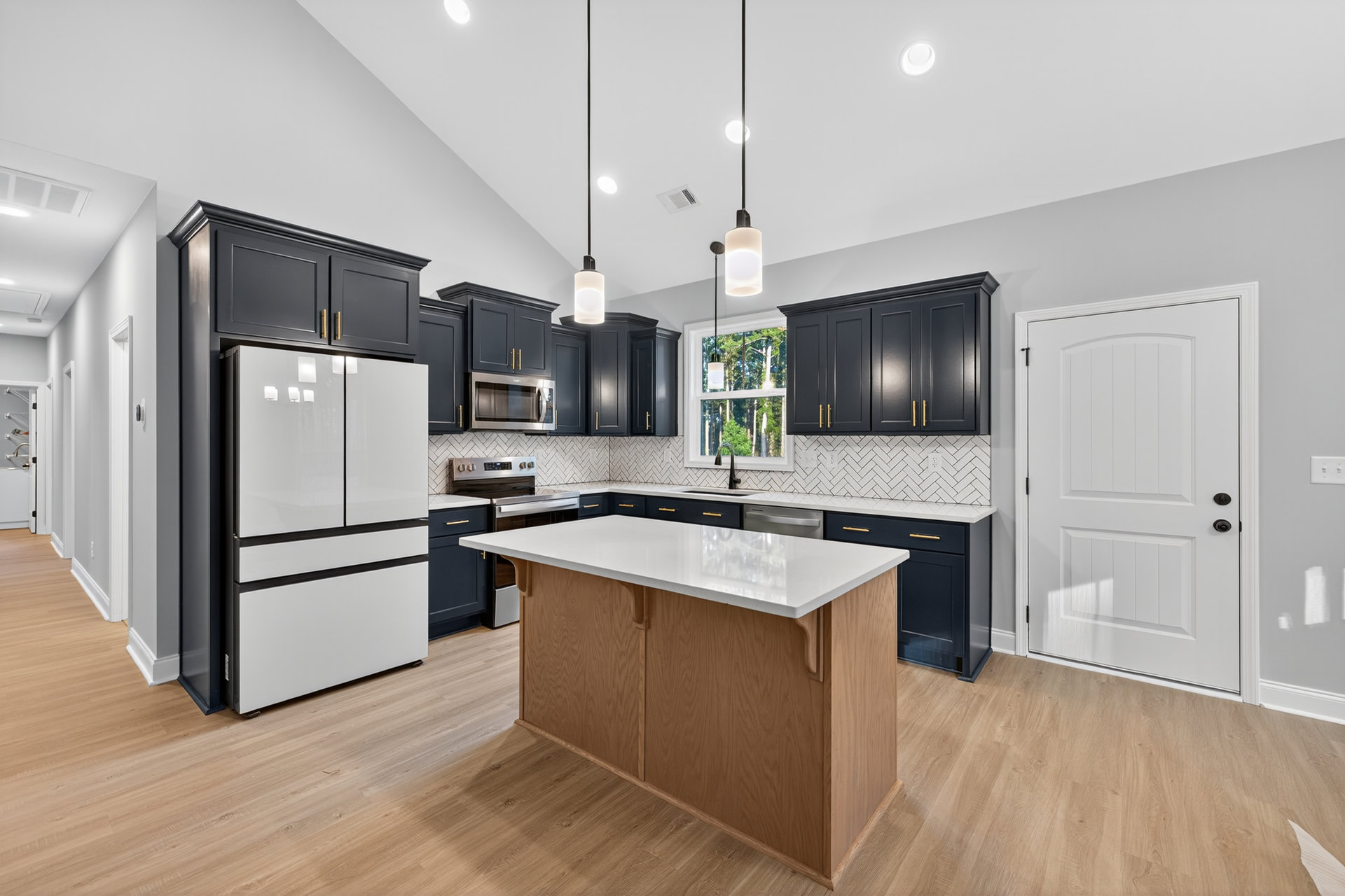 Black lower cabinets and white upper cabinets in a kitchen with a white refrigerator, white countertop, stainless steel microwave, and white door with black hardware