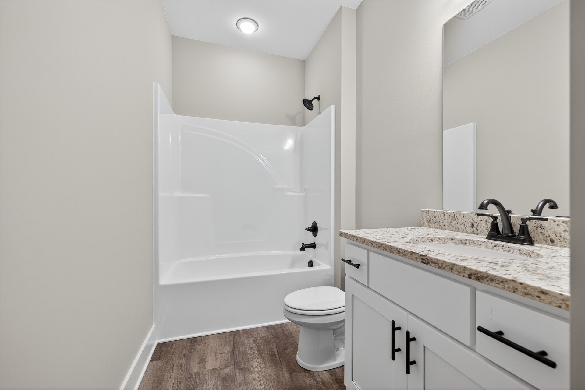 Modern bathroom with white tile walls, white bathtub, black shower head, white toilet with closed seat, white sink, and recessed ceiling light