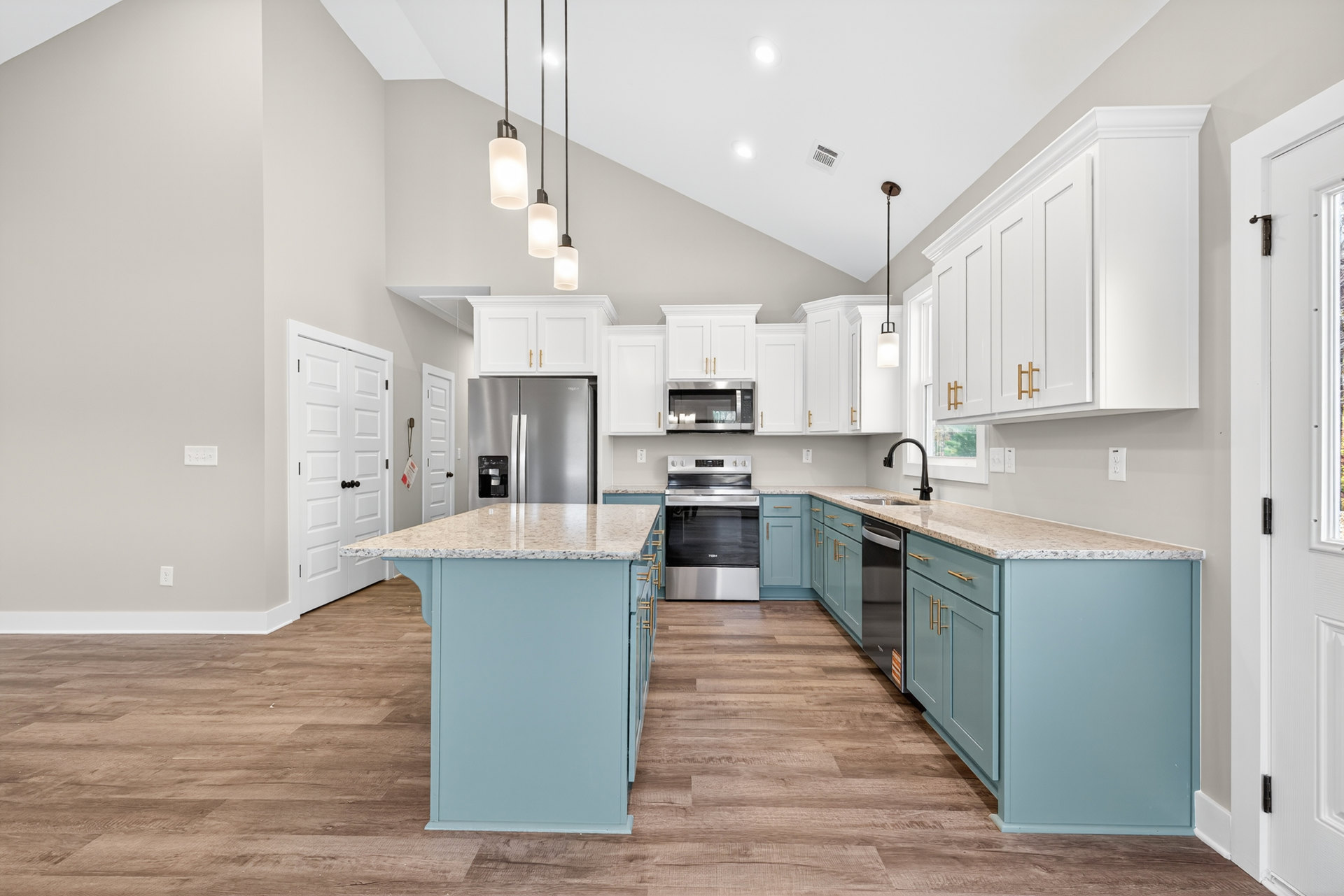 Spacious kitchen featuring a marble-topped island, stainless steel refrigerator and stove, white cabinetry, pendant lighting, and wood flooring