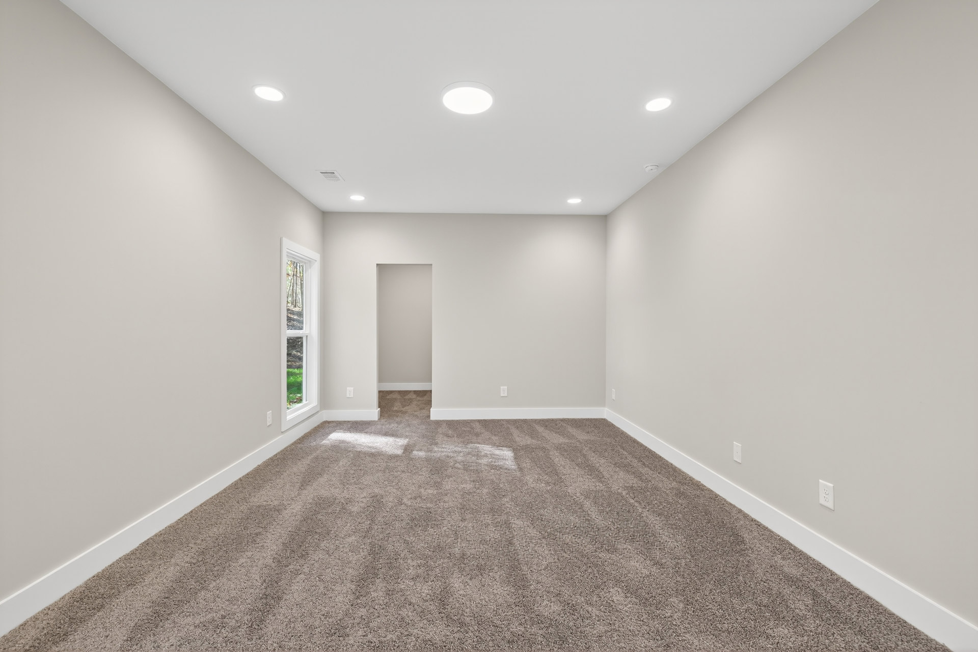 Carpeted room with white walls, recessed ceiling lights, large window with white frame, and white pillow on the floor