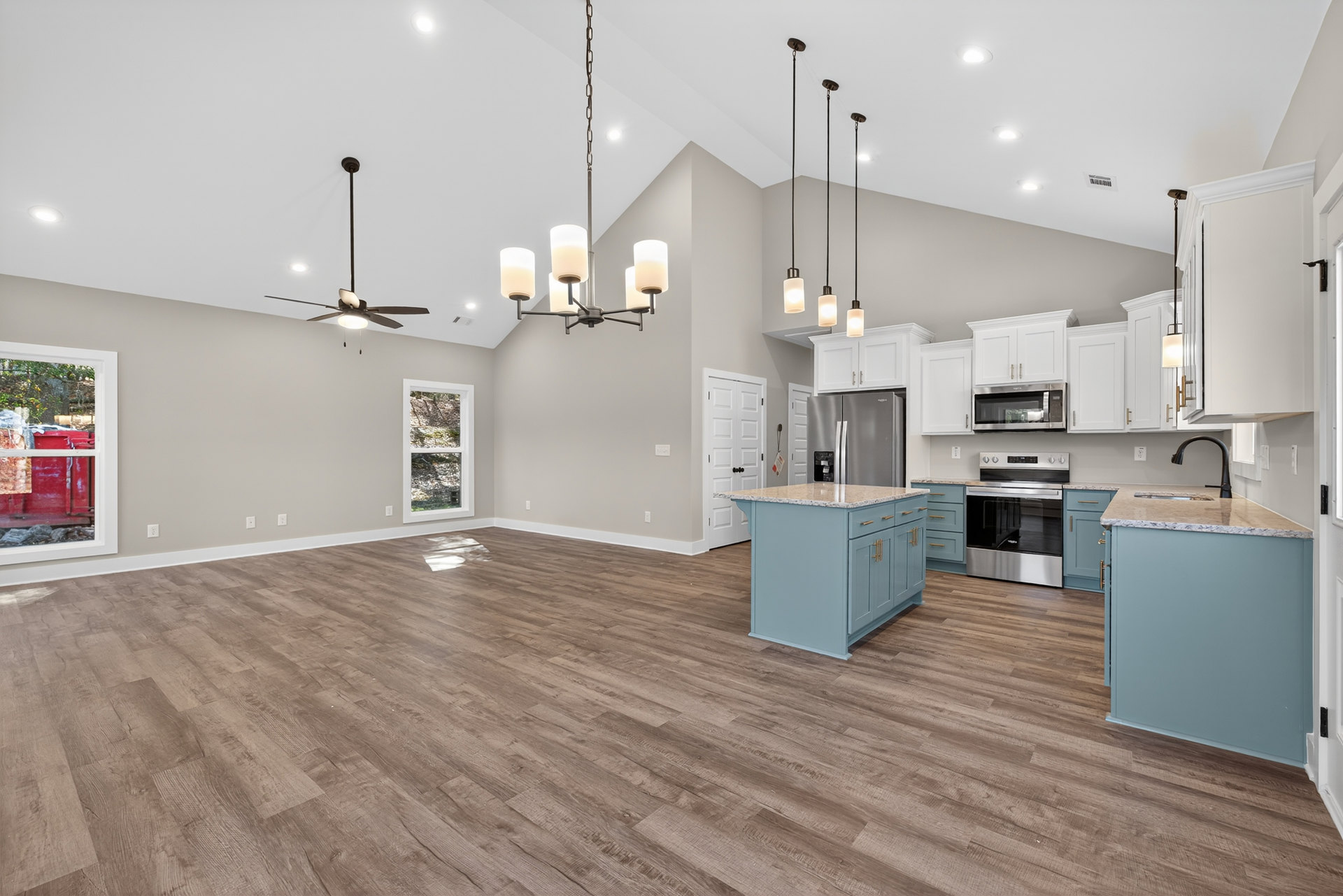 Spacious kitchen featuring wood flooring, marble-topped island, ceiling fan, white-framed window, glass door microwave, and stainless steel stove with cabinetry and sink.