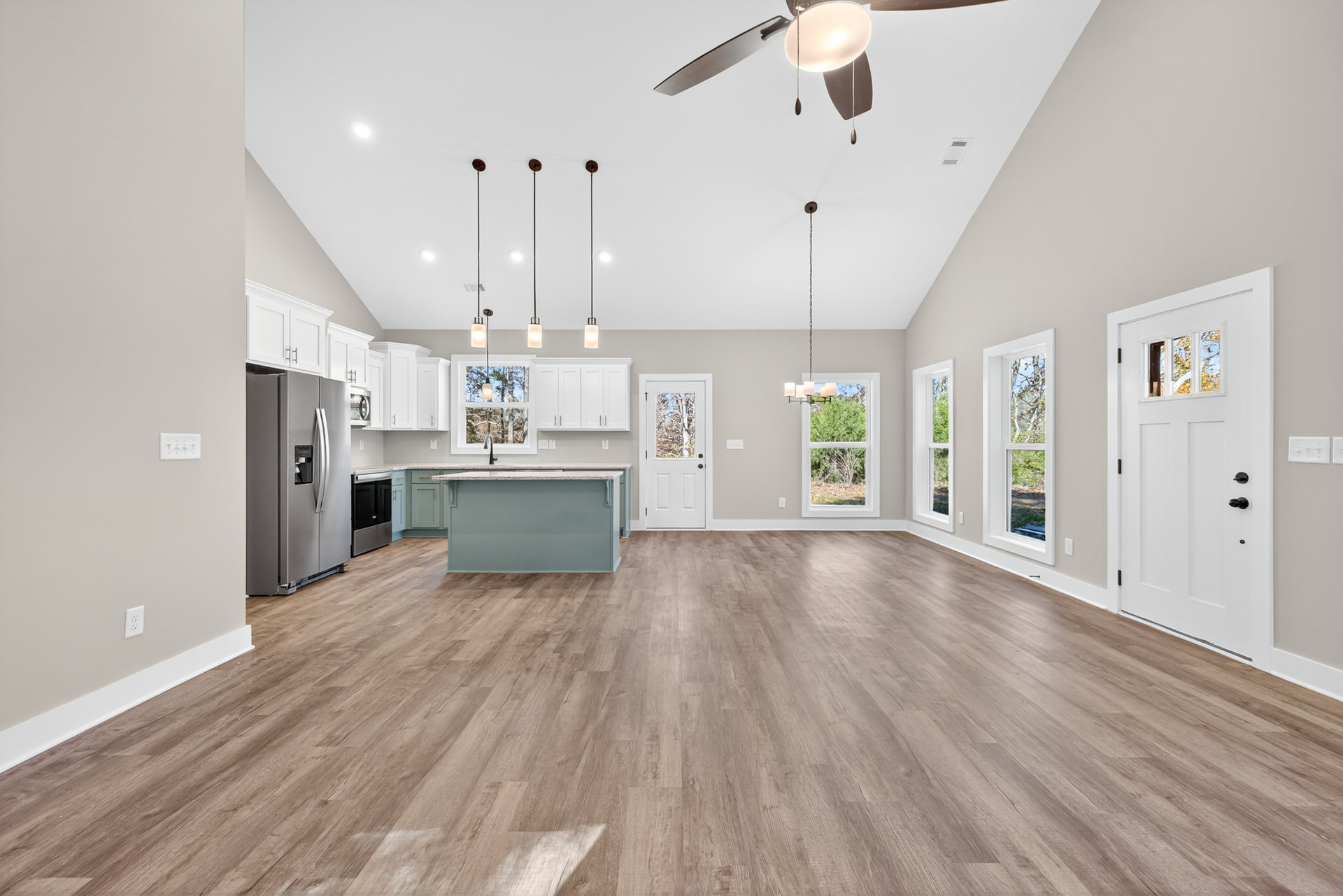 Spacious open floor plan featuring wood flooring, central kitchen island, black refrigerator, white door with window, and large window with white frame