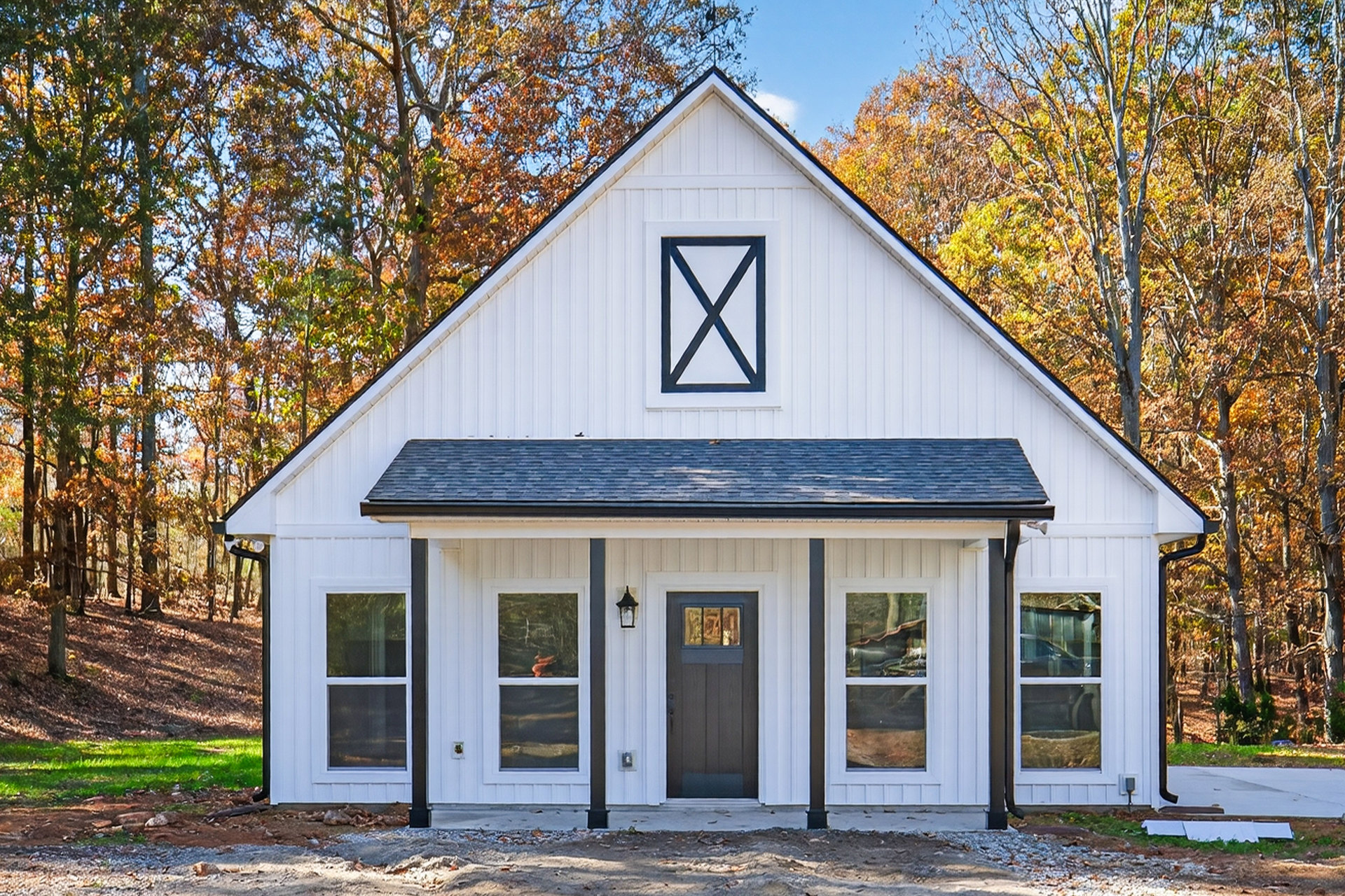 White siding house with black roof, black framed windows, and black front door, surrounded by mature trees and green lawn under blue sky