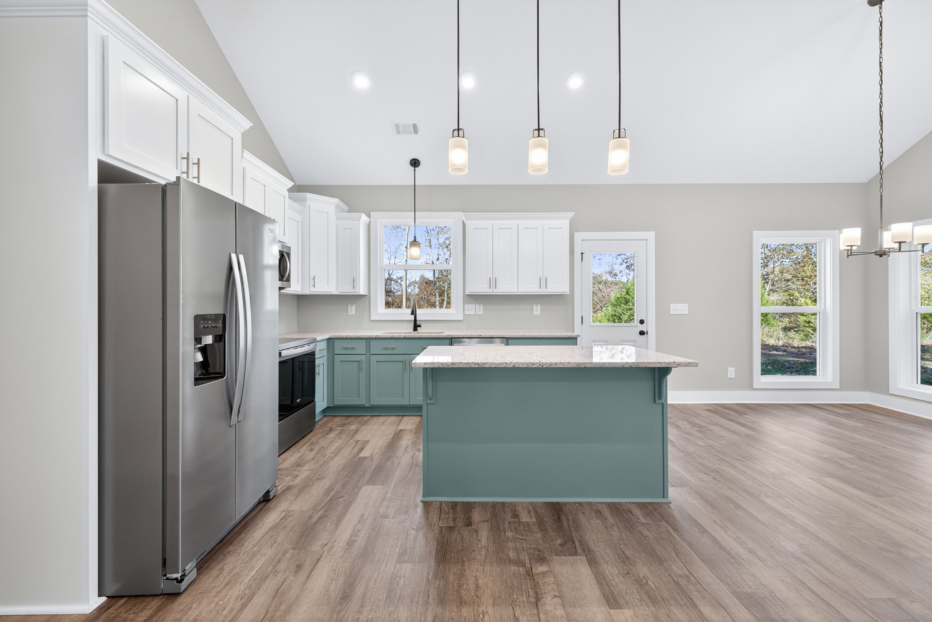 Spacious kitchen featuring a large white island, wood laminate flooring, stainless refrigerator with water dispenser, white countertops, cabinetry, and windows overlooking leafy