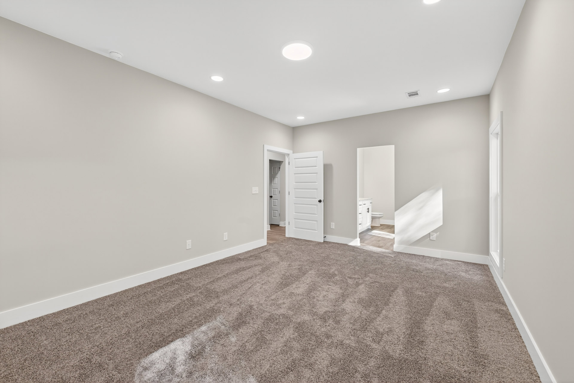Carpeted room with white walls, white ceiling light, white door with black knob, and wall-mounted mirror