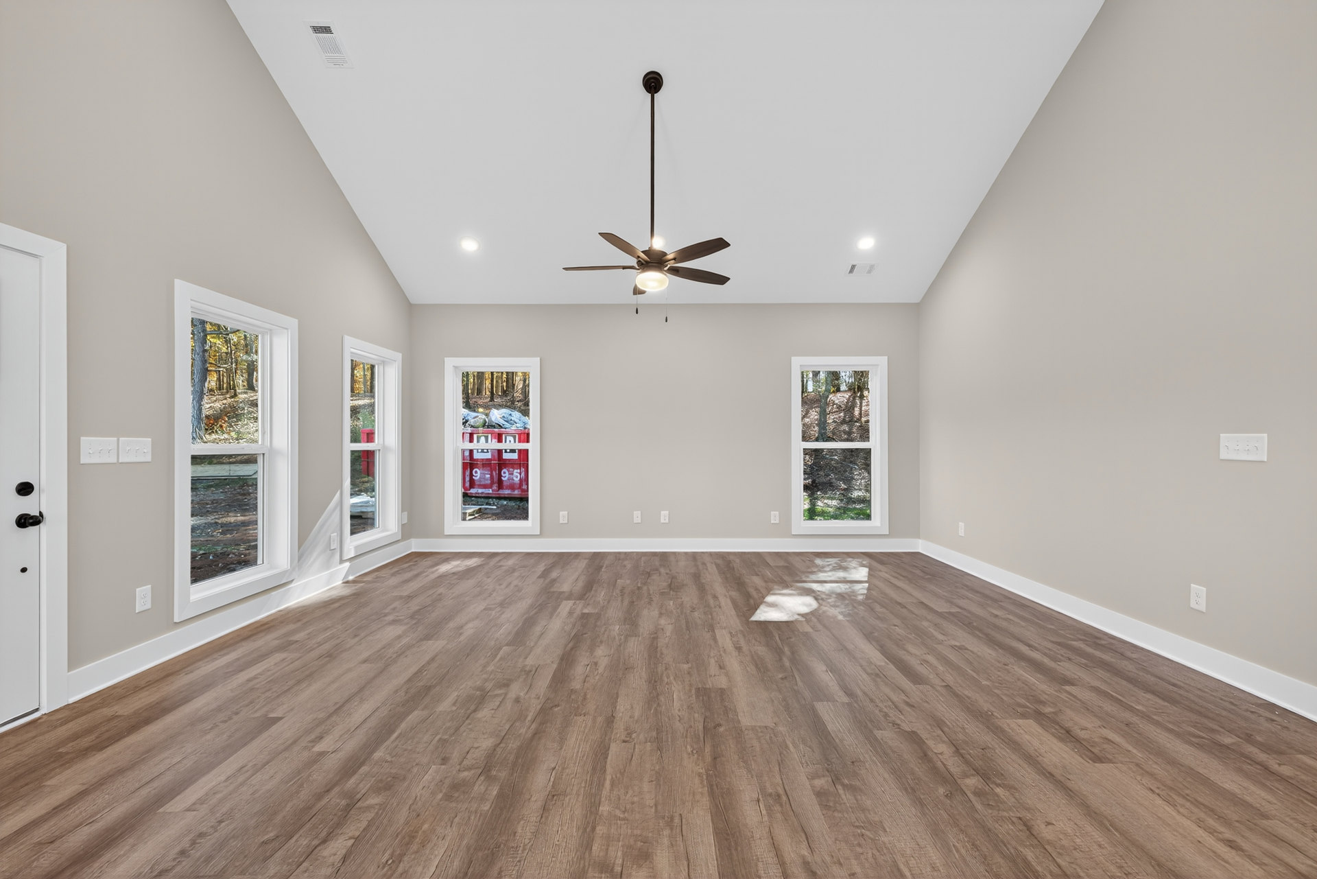 Ceiling fan with light fixture, wood flooring with white baseboards, two windows with white frames, red container with numbers and letters on windowsill, tree trunk visible outside