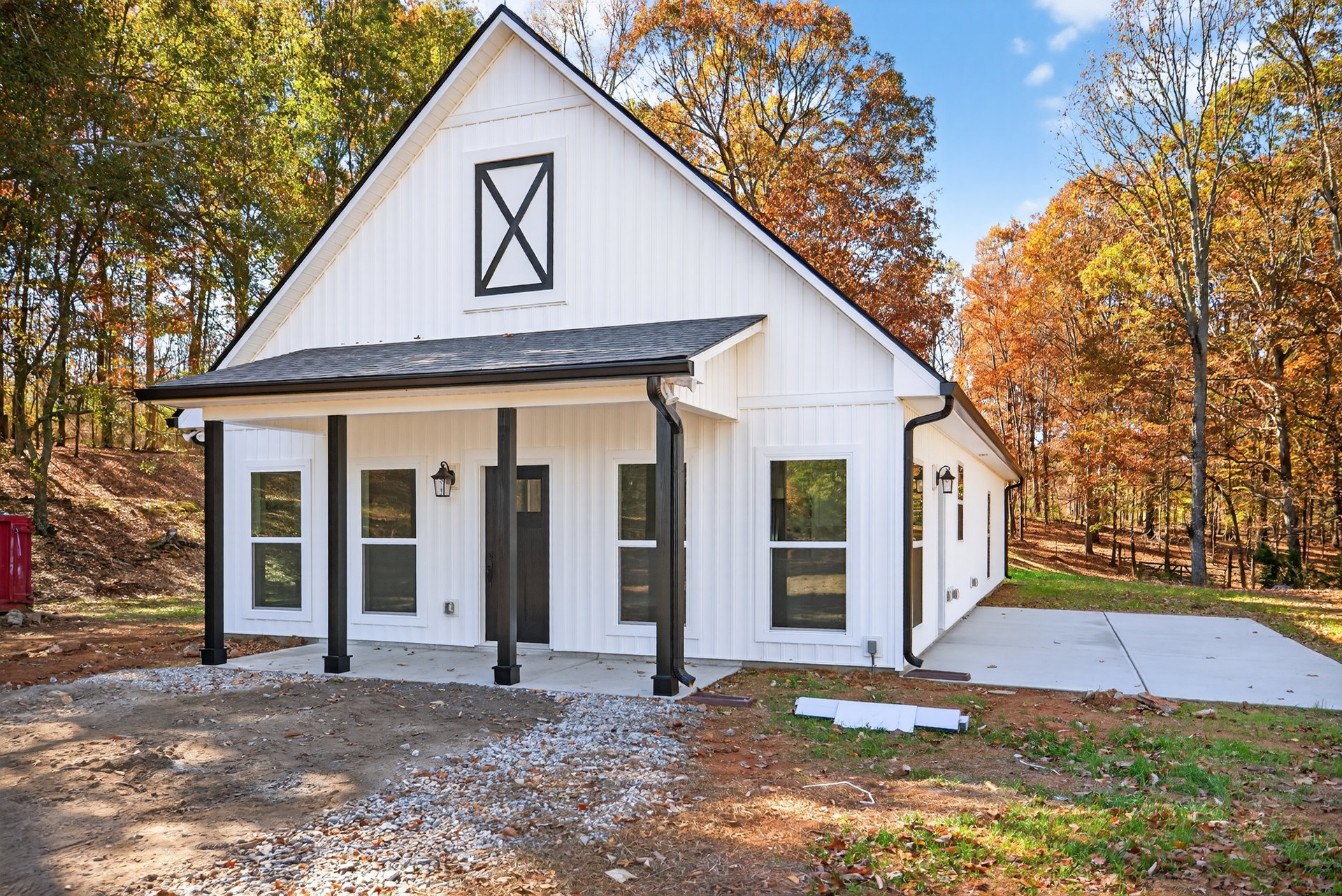 White two-story house with black pillars, white framed windows, and trees in the background; close-up of roof and autumn foliage visible.
