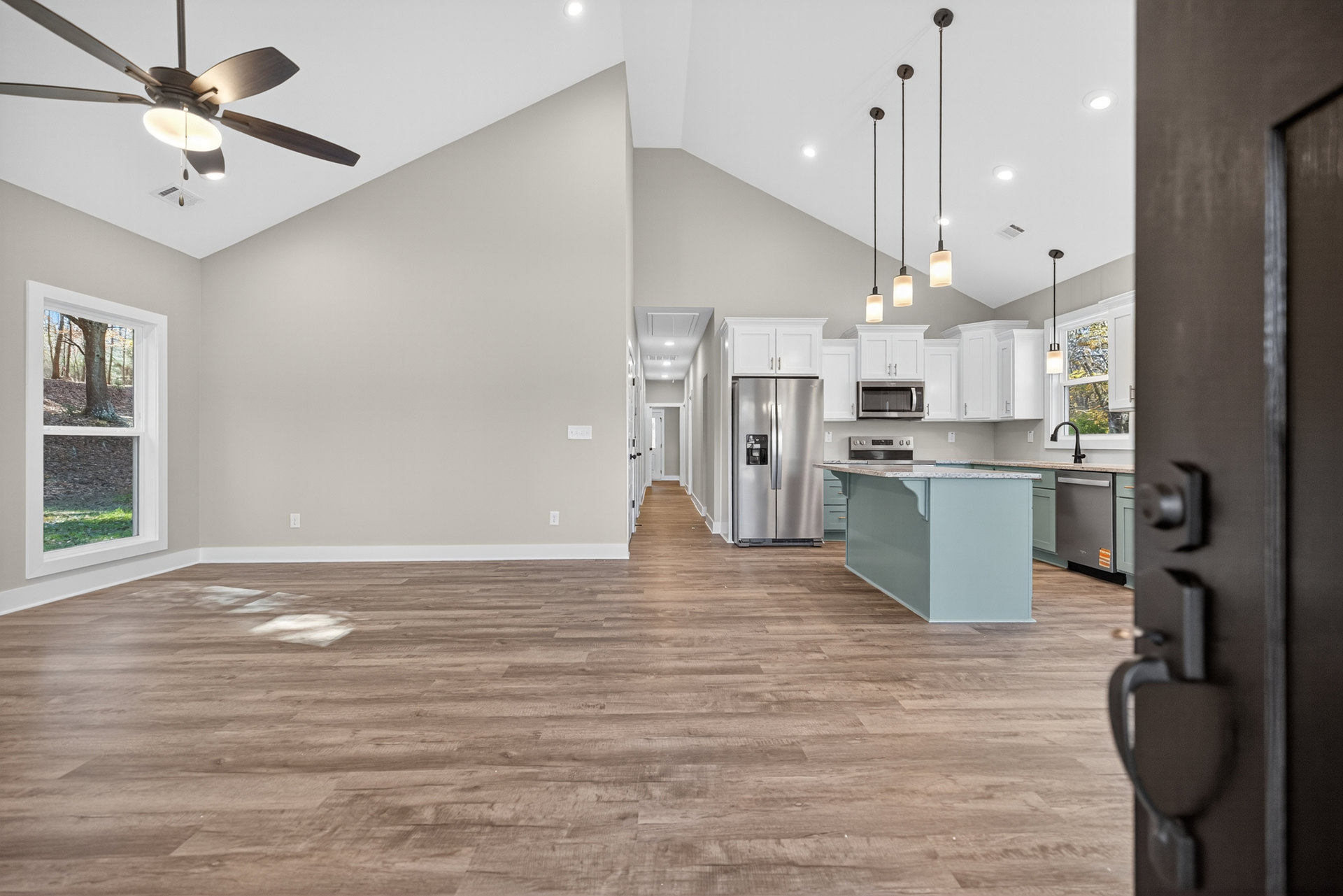 Open-concept kitchen and living room featuring laminate flooring, marble-topped island, stainless steel refrigerator and microwave, white cabinetry, ceiling fan with light, and