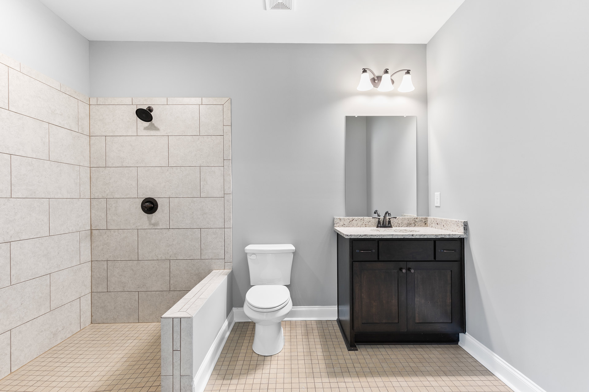Bathroom with white toilet, marble countertop sink, round black shower head, chrome faucet knob, and modern light fixture against tiled walls.