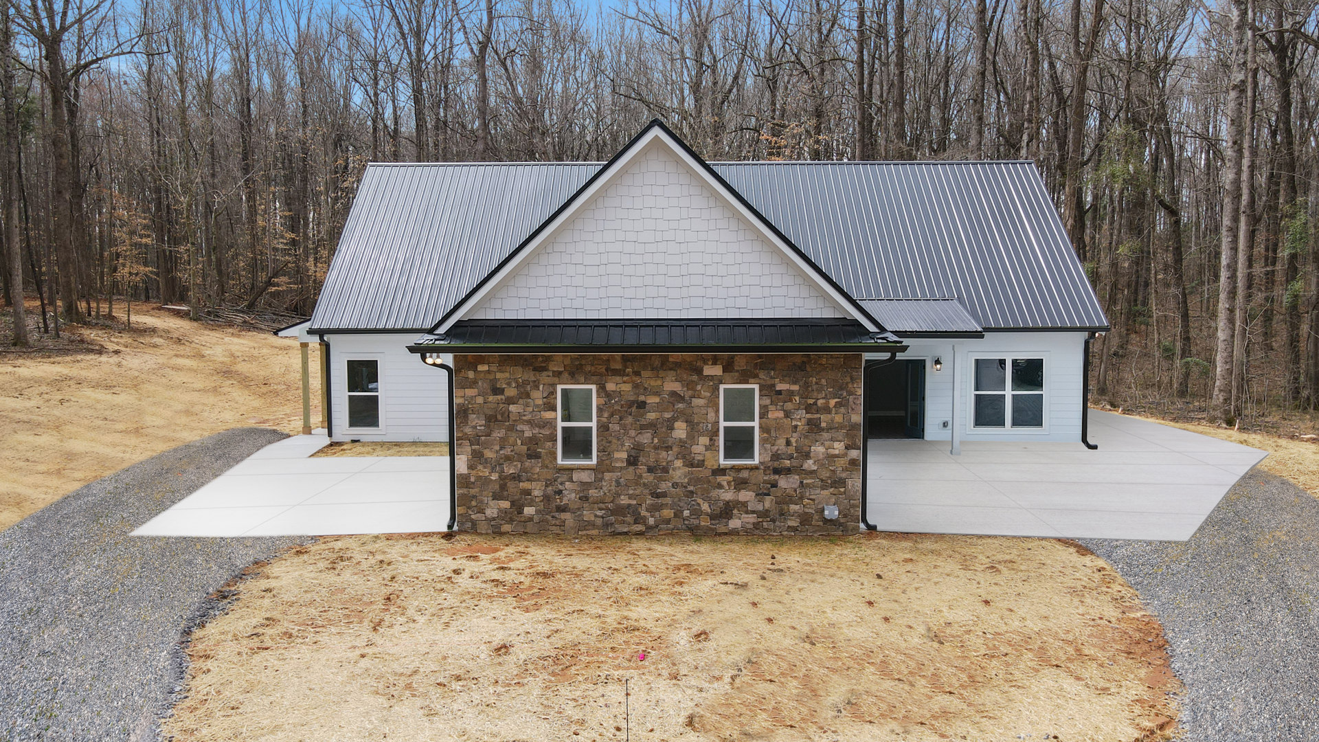 Modern home exterior with white-framed windows, stone wall, dry grass landscaping, paved driveway, and wooden fence