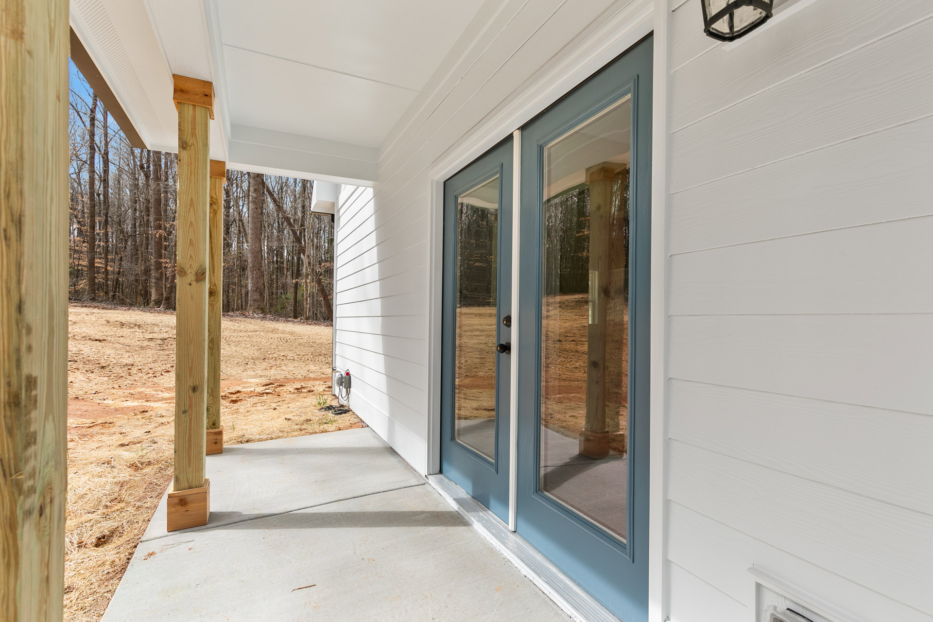 White siding exterior with blue front door, glass-paneled porch doors, wooden post in landscaped yard, close-up details of wood block, plank, and glass window