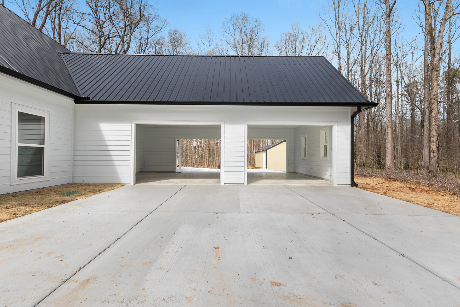 White house with black roof, large windows, white concrete entry, wood-paneled accent wall, small shed nearby, surrounded by bare trees