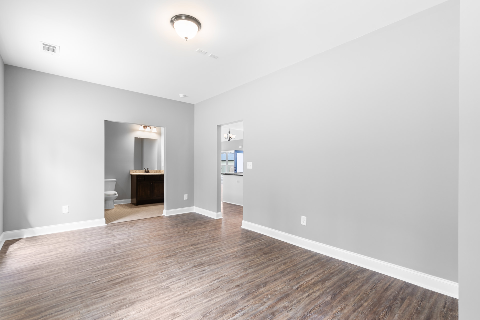 Bathroom with wood flooring, white trim, white toilet, modern sink, and a contemporary light fixture.
