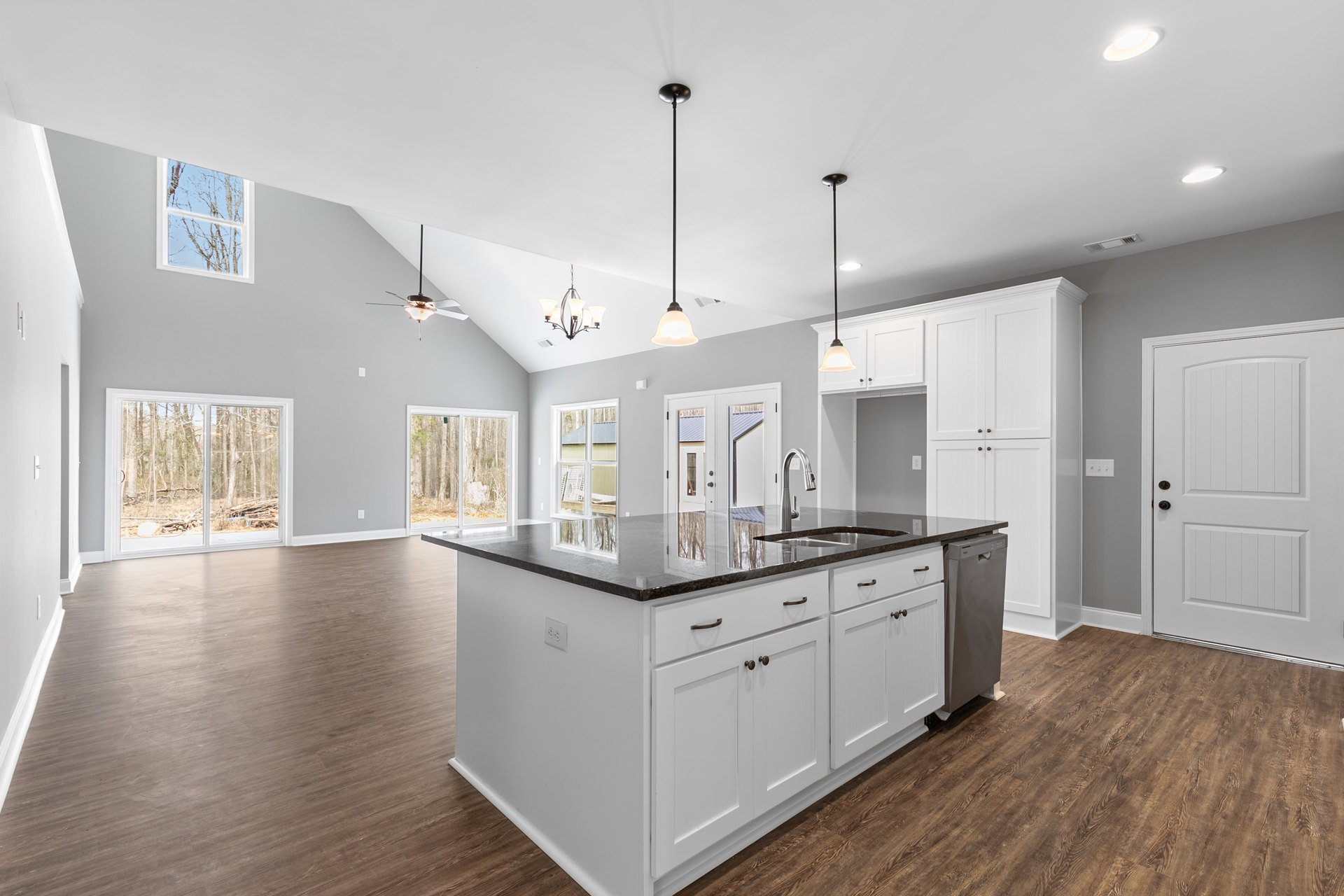 Open kitchen and dining area featuring wood flooring, white cabinetry on the kitchen island with black countertops, a white door with black handle, black support pole, and large