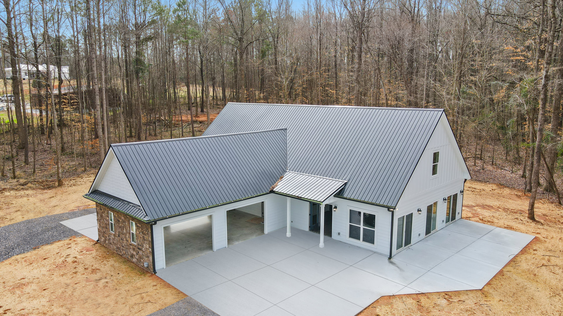 White two-story house with covered front porch, attached garage, paved driveway, and mature trees in the background
