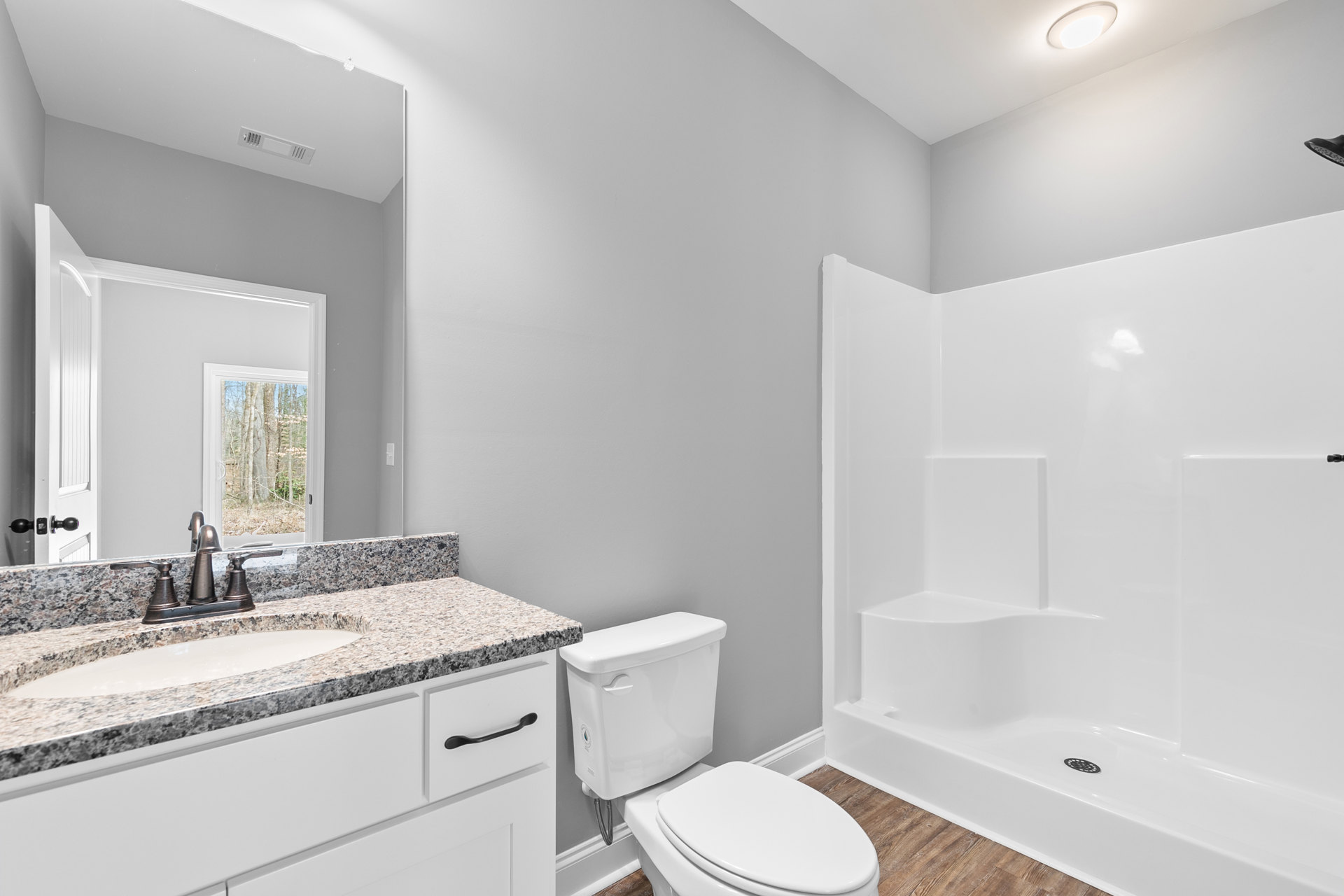 Bathroom with white toilet, marble countertop sink, wooden flooring, tiled walls, and chrome faucet