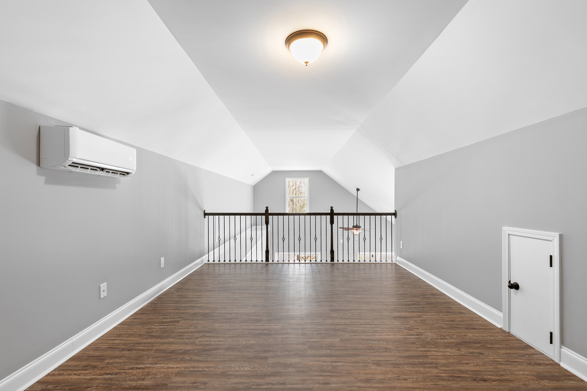 Wood floor with metal railing, white door with black handle, modern ceiling light fixture, smooth plaster walls
