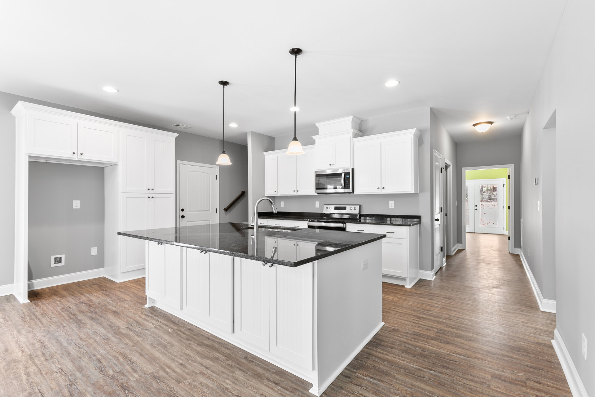 Kitchen with black countertop, white cabinets with silver knobs, kitchen island featuring a sink, microwave oven with glass door, door with glass panes, black pole light fixture in