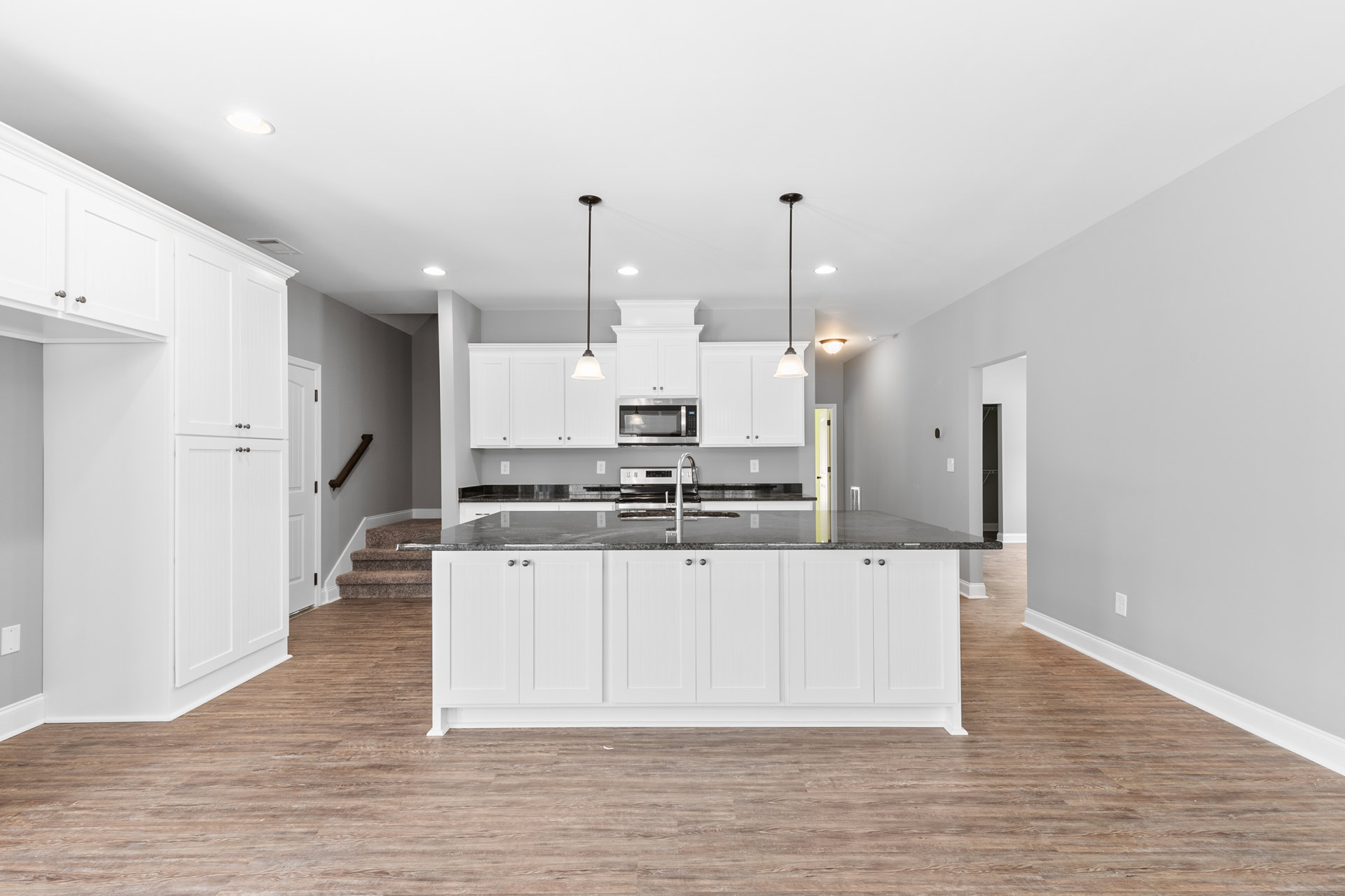 Spacious kitchen featuring a large white island with built-in sink, white cabinetry, light wood flooring, and stainless steel appliances.