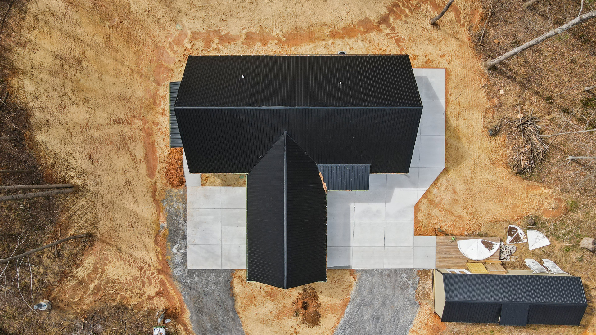 Modern home exterior with black shingle roof, white siding, and landscaped front yard with tree branches on the ground