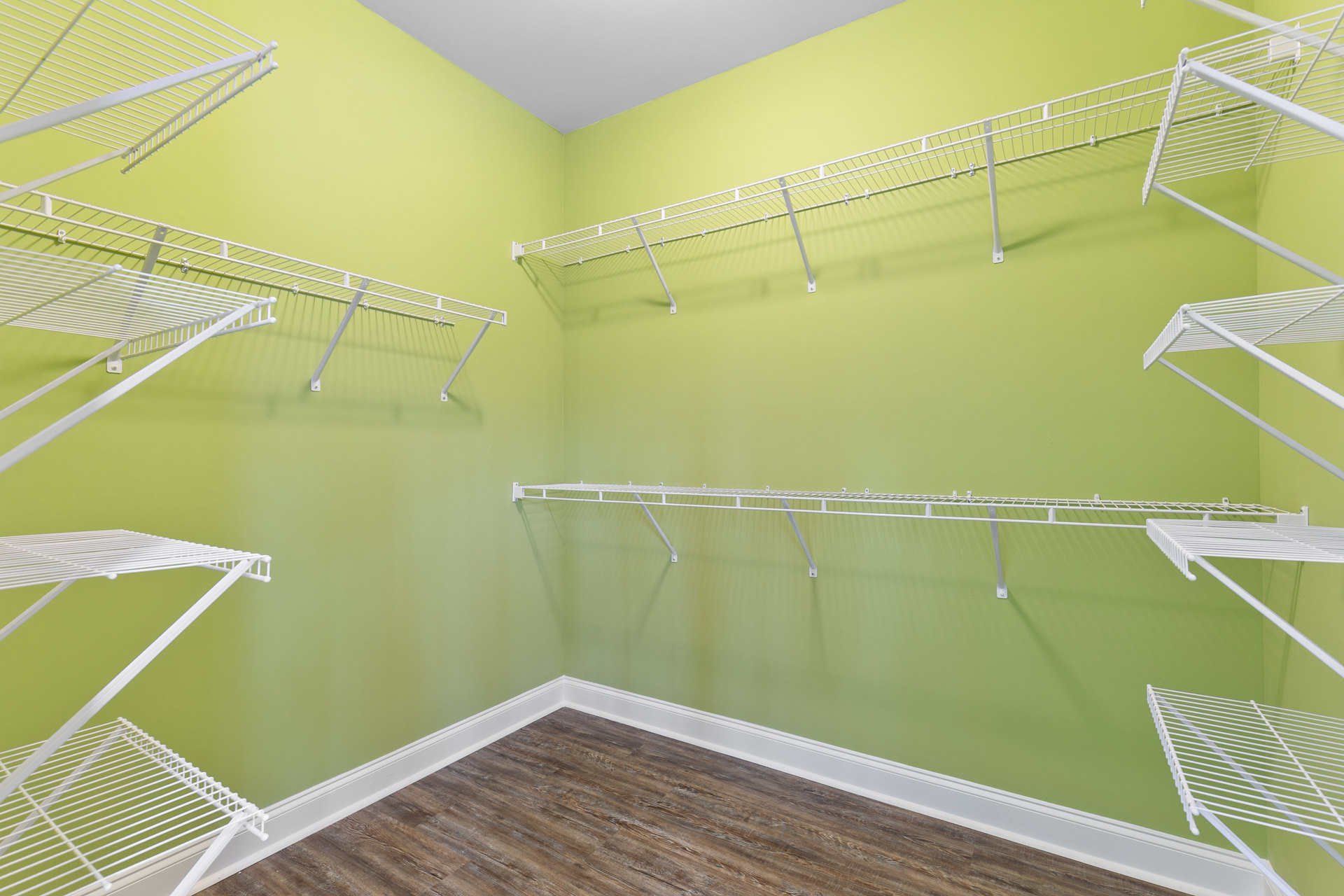 Green accent wall with built-in white shelves, white clothes rack, wood flooring, and white baseboard trim