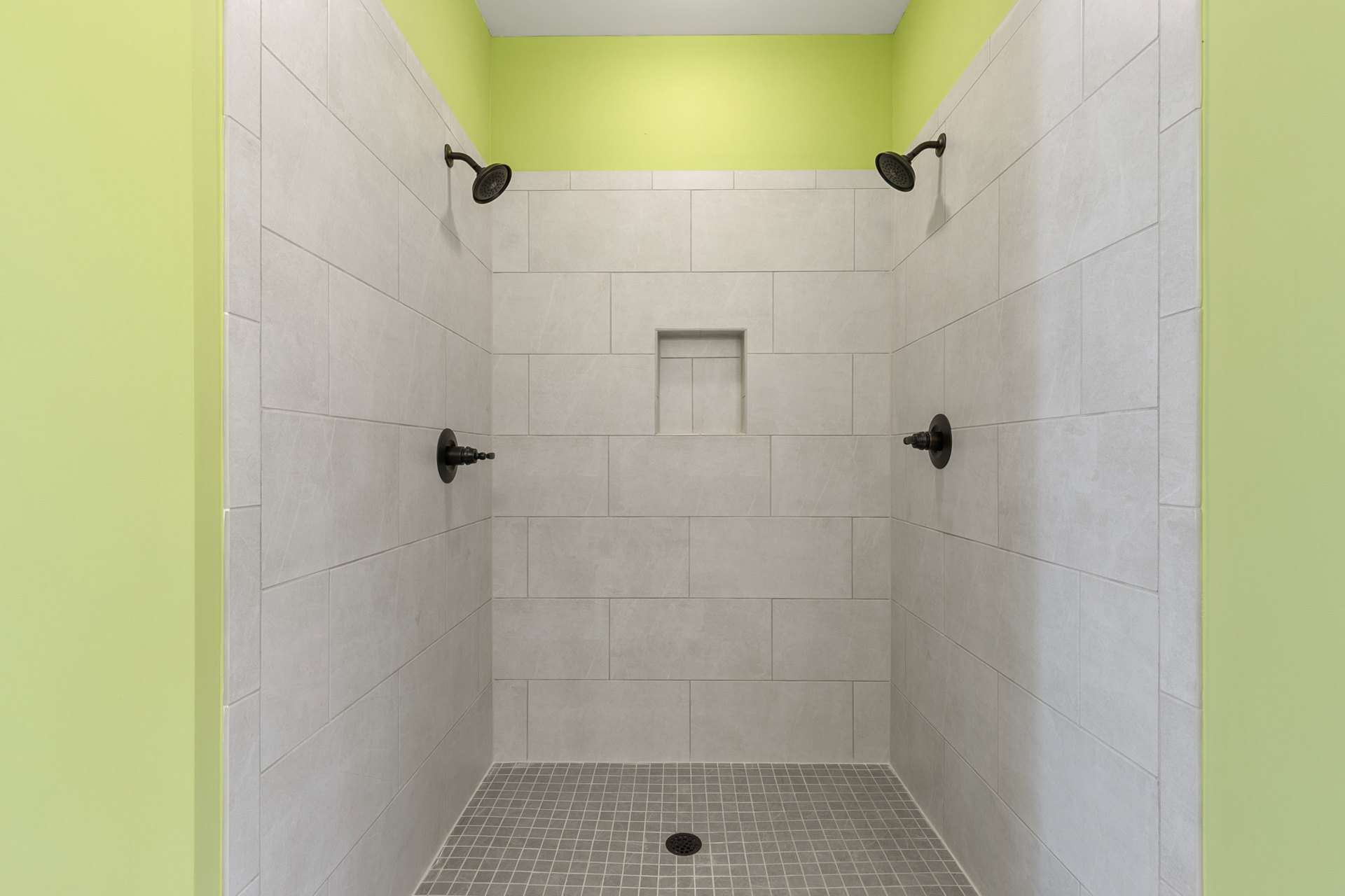 Shower with green ceiling, white tile walls, built-in shelf with black handle, silver faucet, wall-mounted shower head, and floor drain
