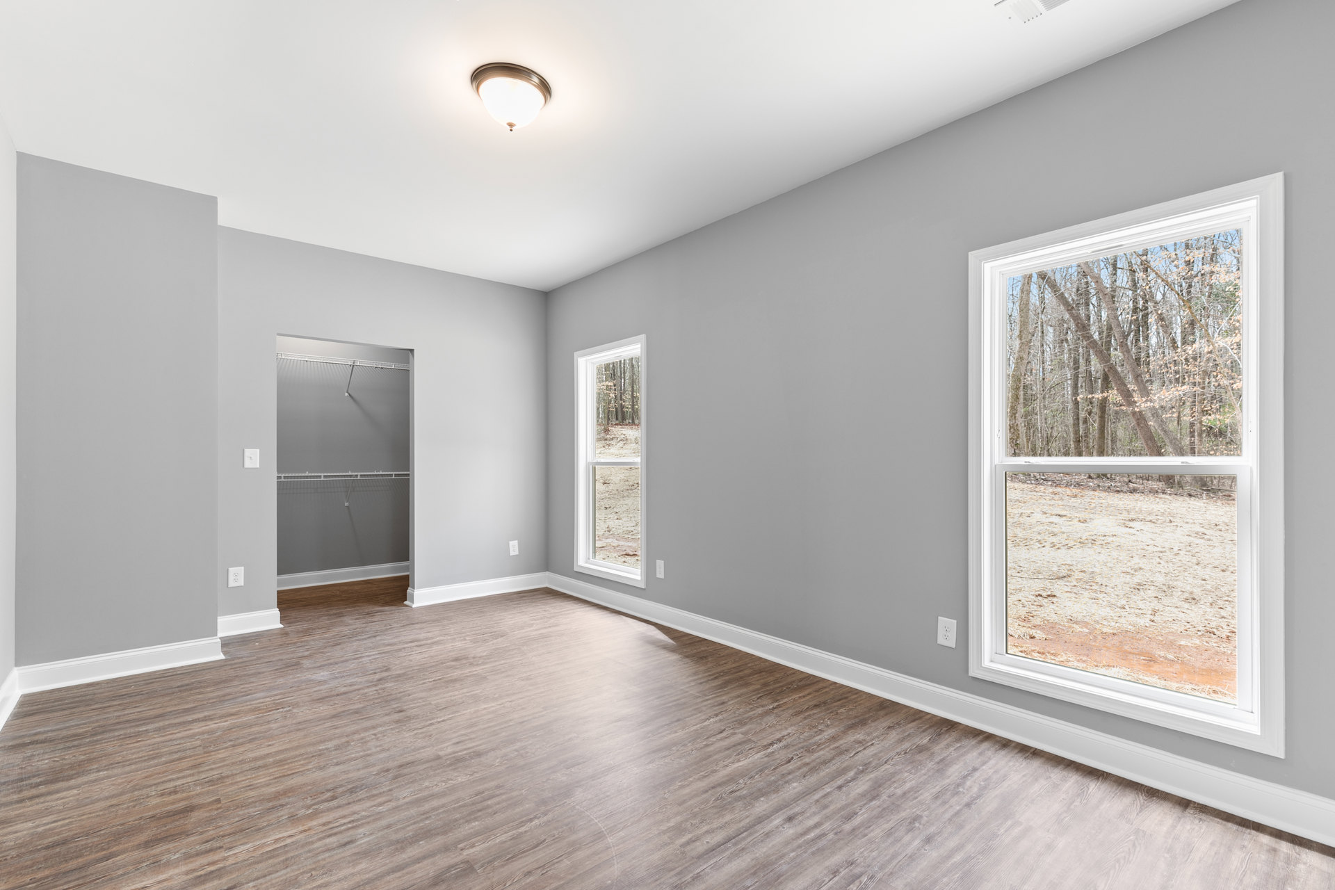 Bedroom with wood flooring, built-in closet, wall-mounted shelf, large window overlooking trees, and a full-length mirror reflecting natural light.