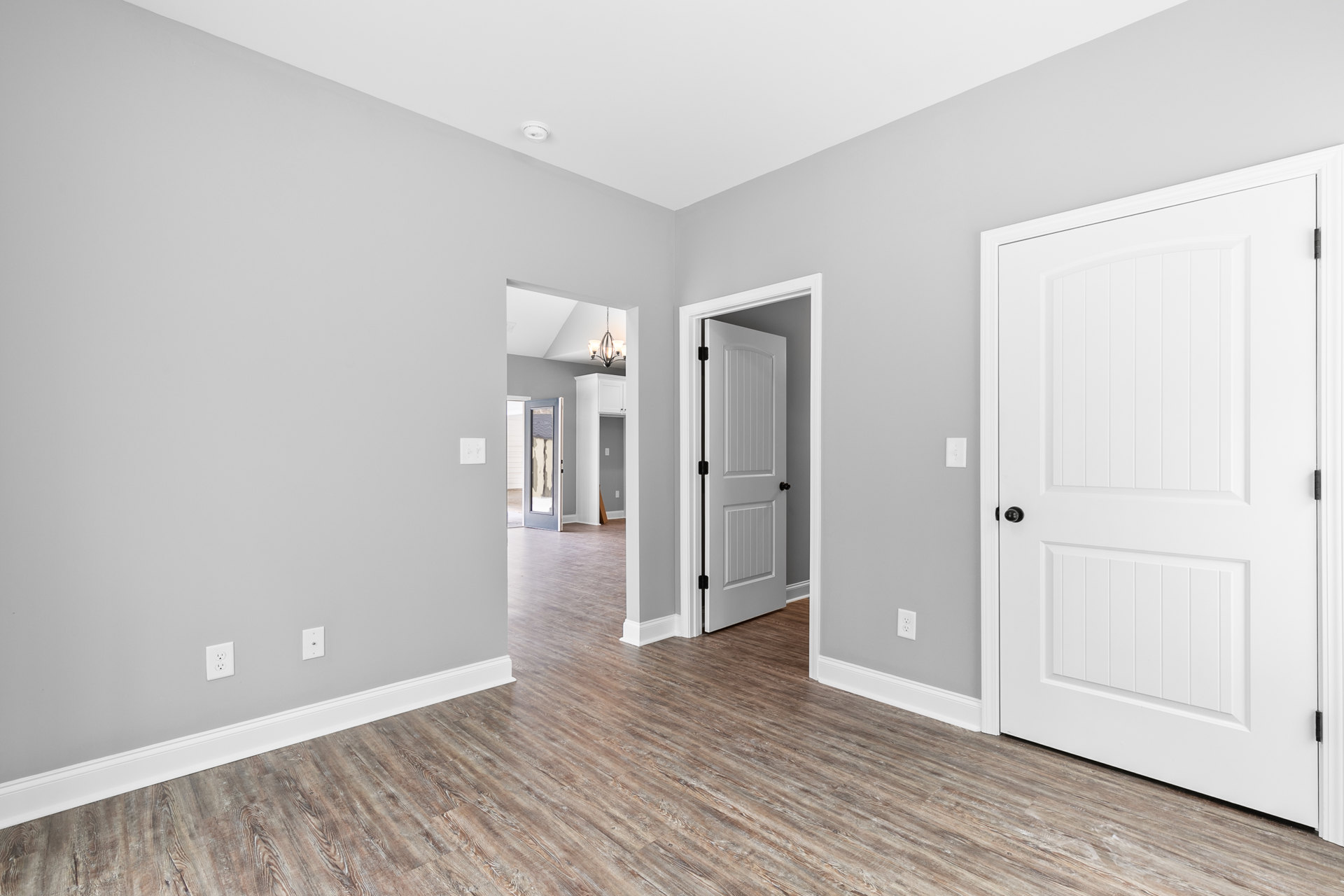 Hardwood floor with white baseboard trim, white paneled doors featuring black knobs, plaster walls, and a window showing a visible crack