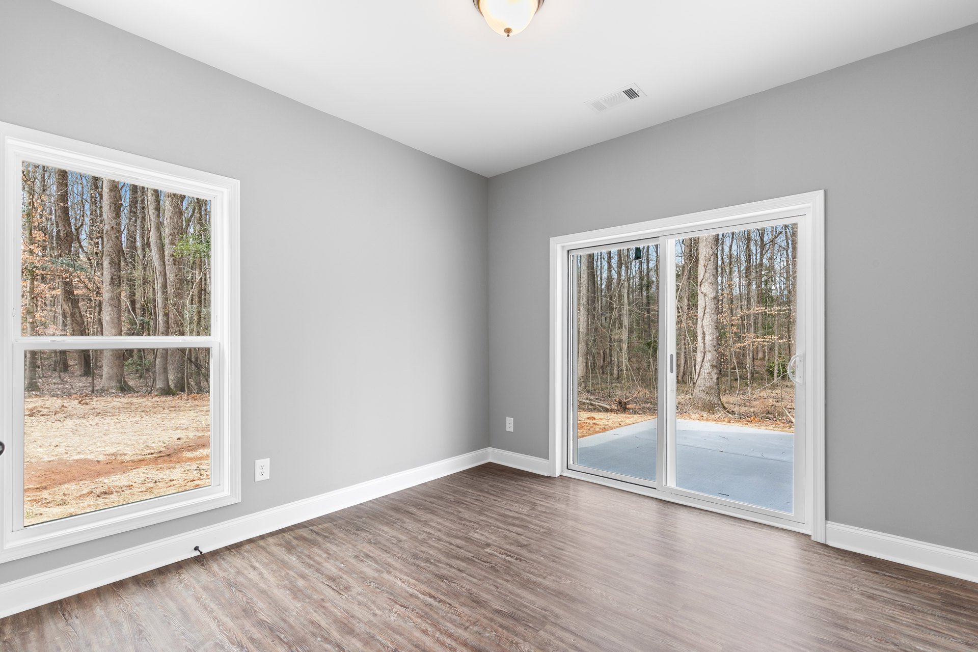 Wood flooring and white ceiling in a room featuring a sliding glass door and windows overlooking trees.