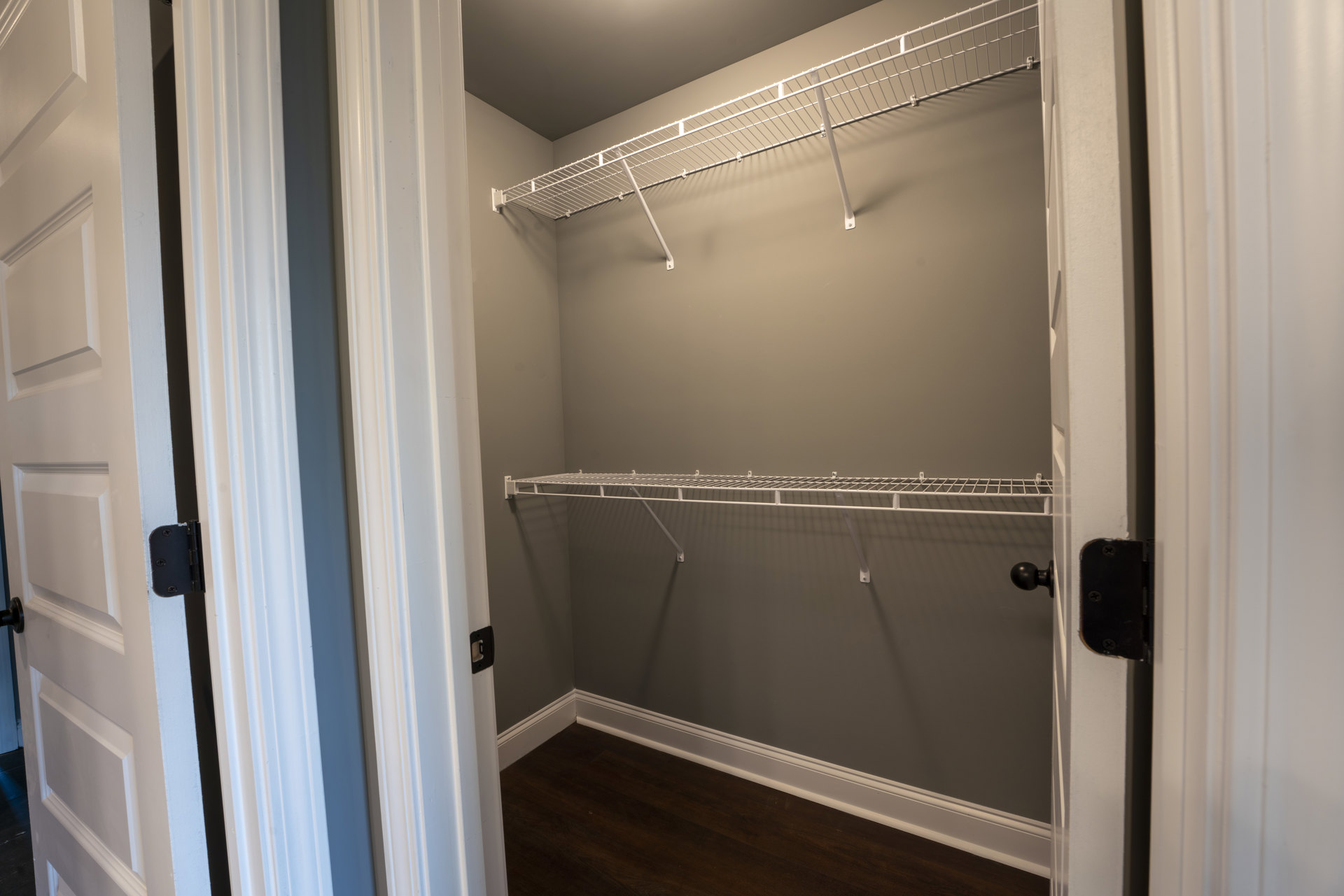 Walk-in closet with built-in white shelves, recessed lighting, dark wood flooring, white baseboards, and a hinged door with black hardware