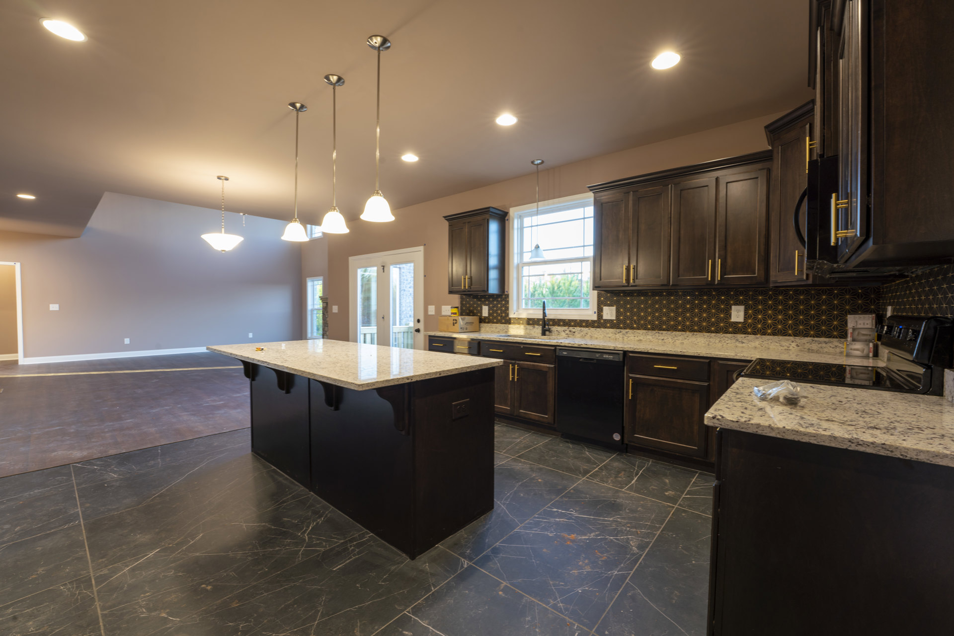 Kitchen with dark wood cabinets, marble countertops, central island, stainless steel sink, tile flooring, ceiling lights, and modern metal light fixture