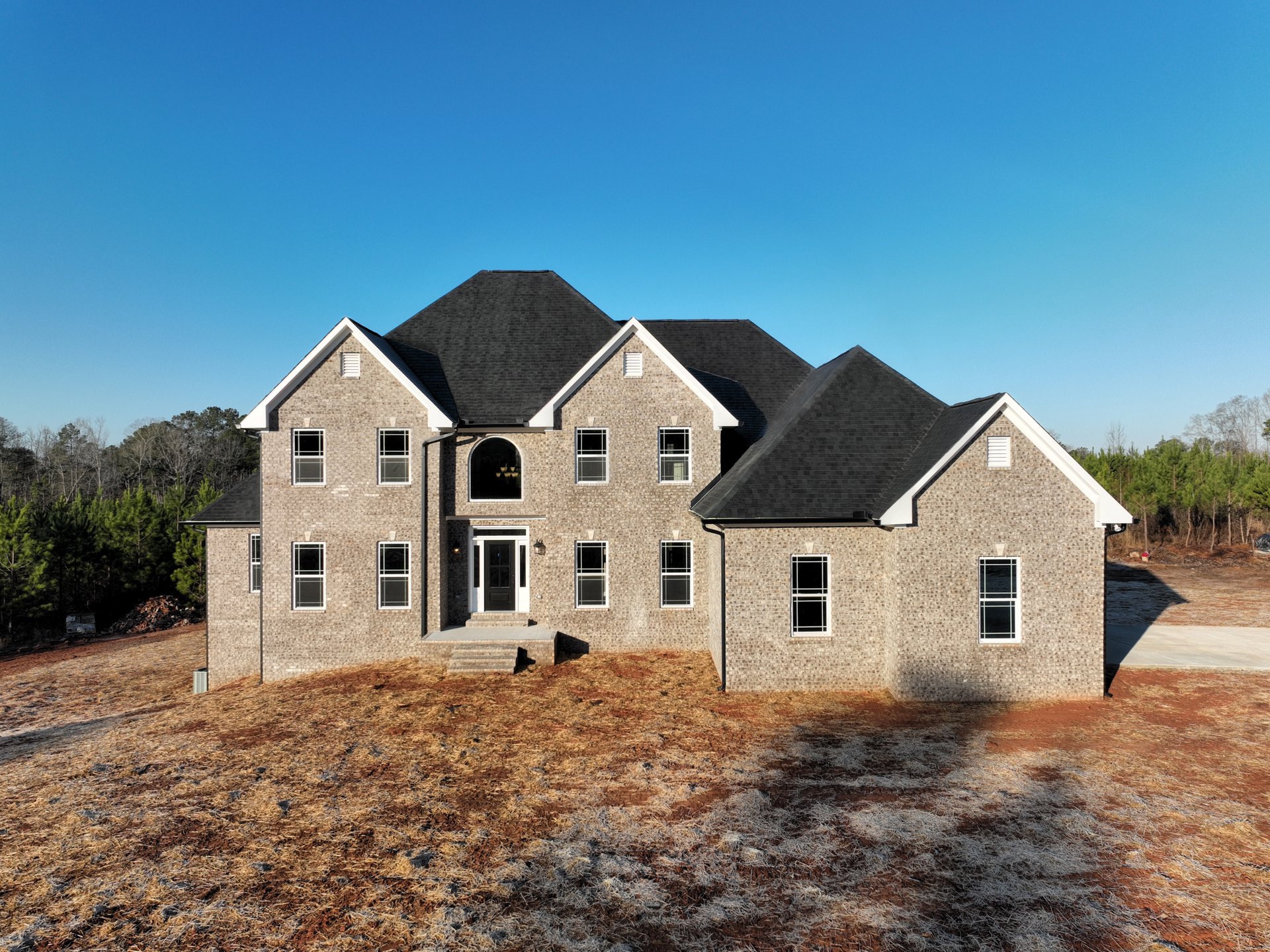 Two-story house with black roof, white siding, black door with white trim, large grassy front yard, mature trees, and a window with broken glass.