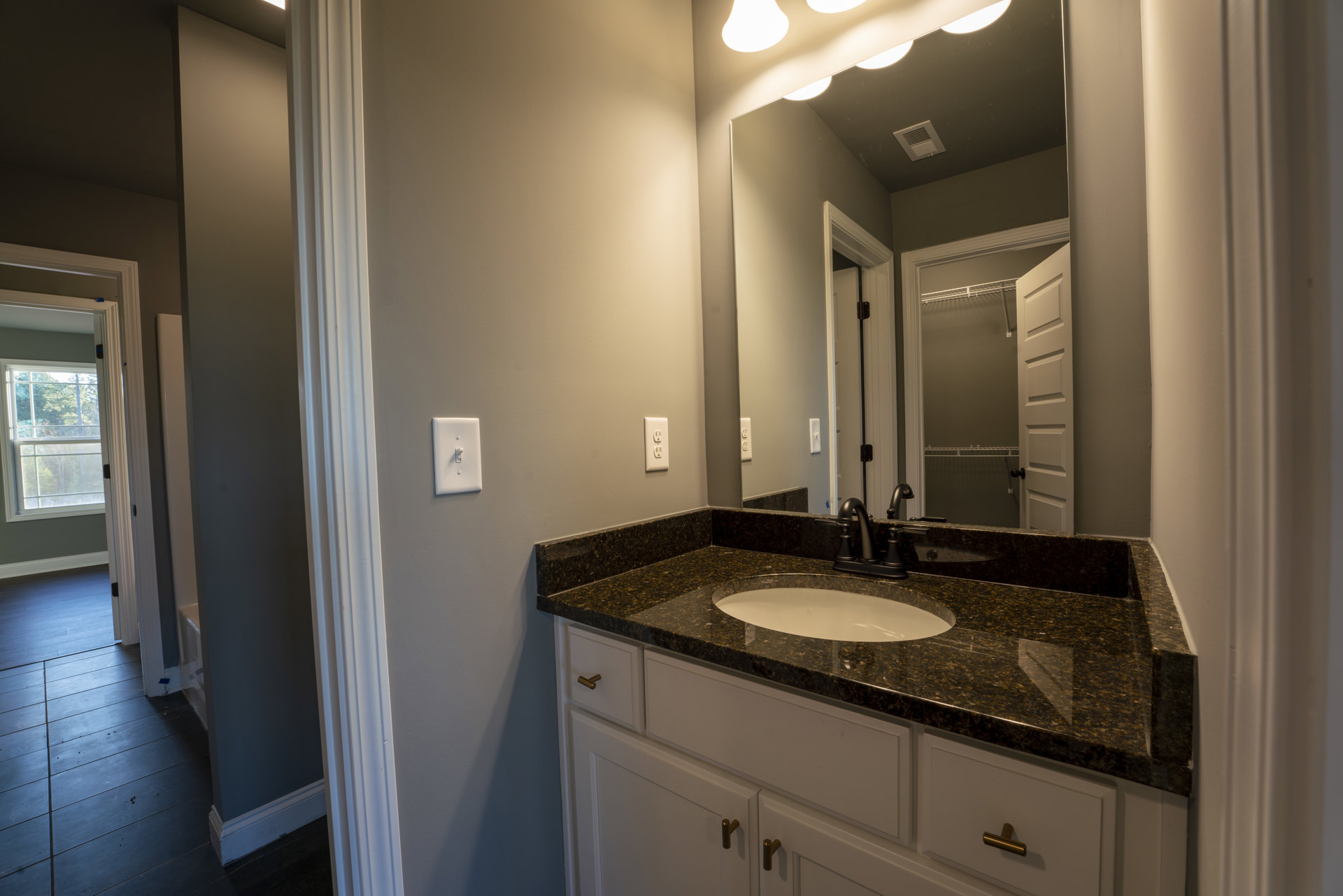 Marble countertop with black faucet and sink, large mirror above, dark wood flooring with crumbs, light switch on wall