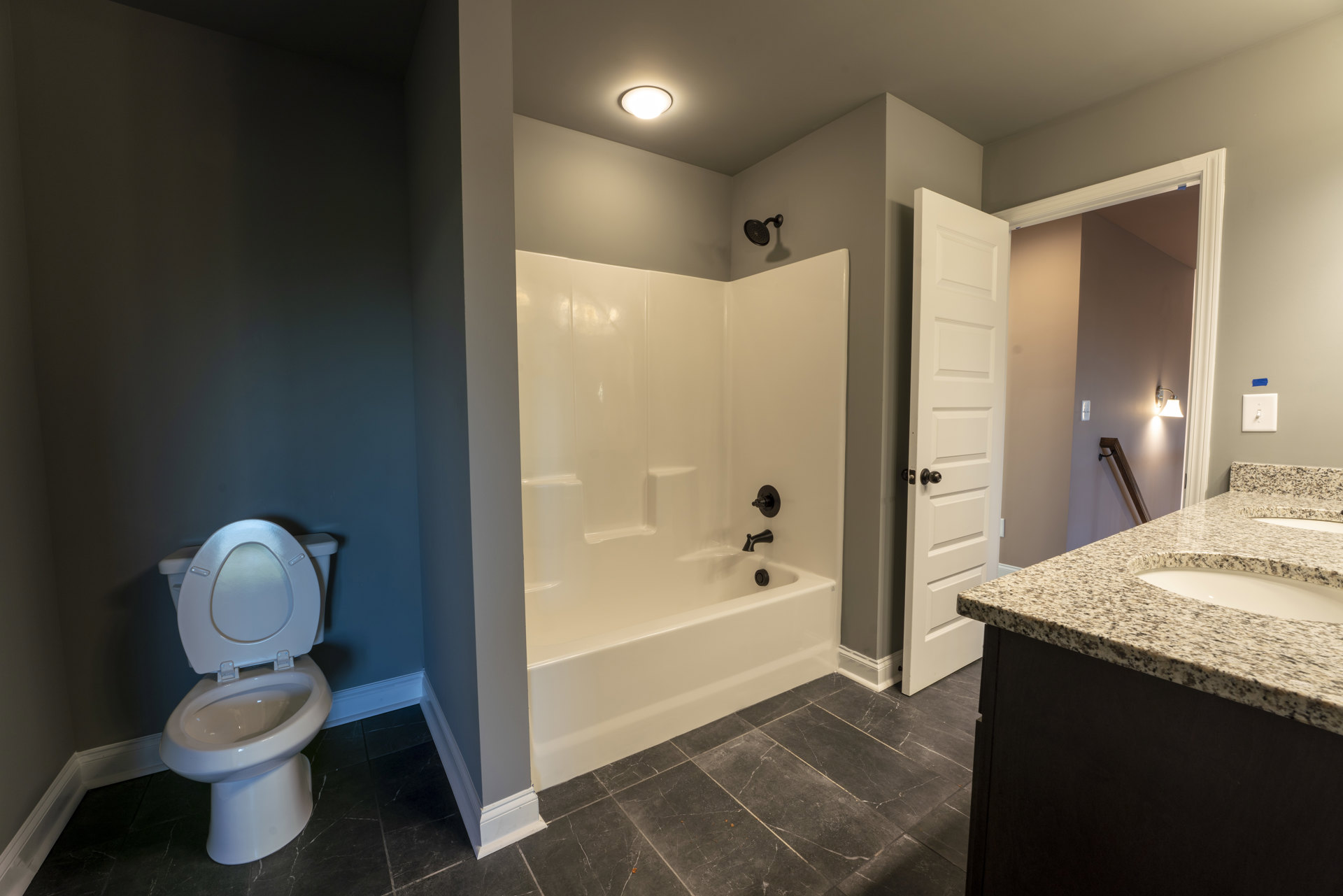 White bathtub and toilet with lid up in a tiled bathroom, overhead light fixture, light switch on wall