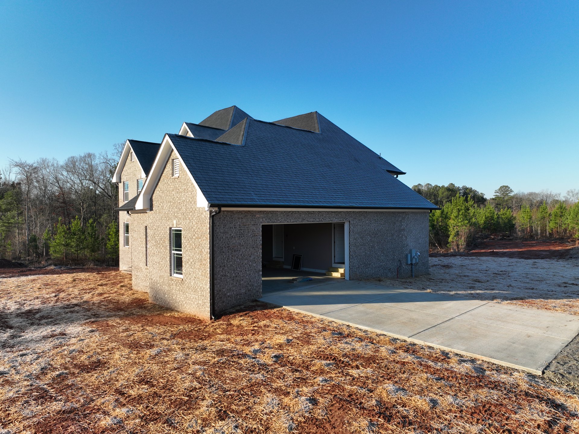 Two-story brick house with attached garage, concrete driveway, and gabled roof, surrounded by trees under a clear sky