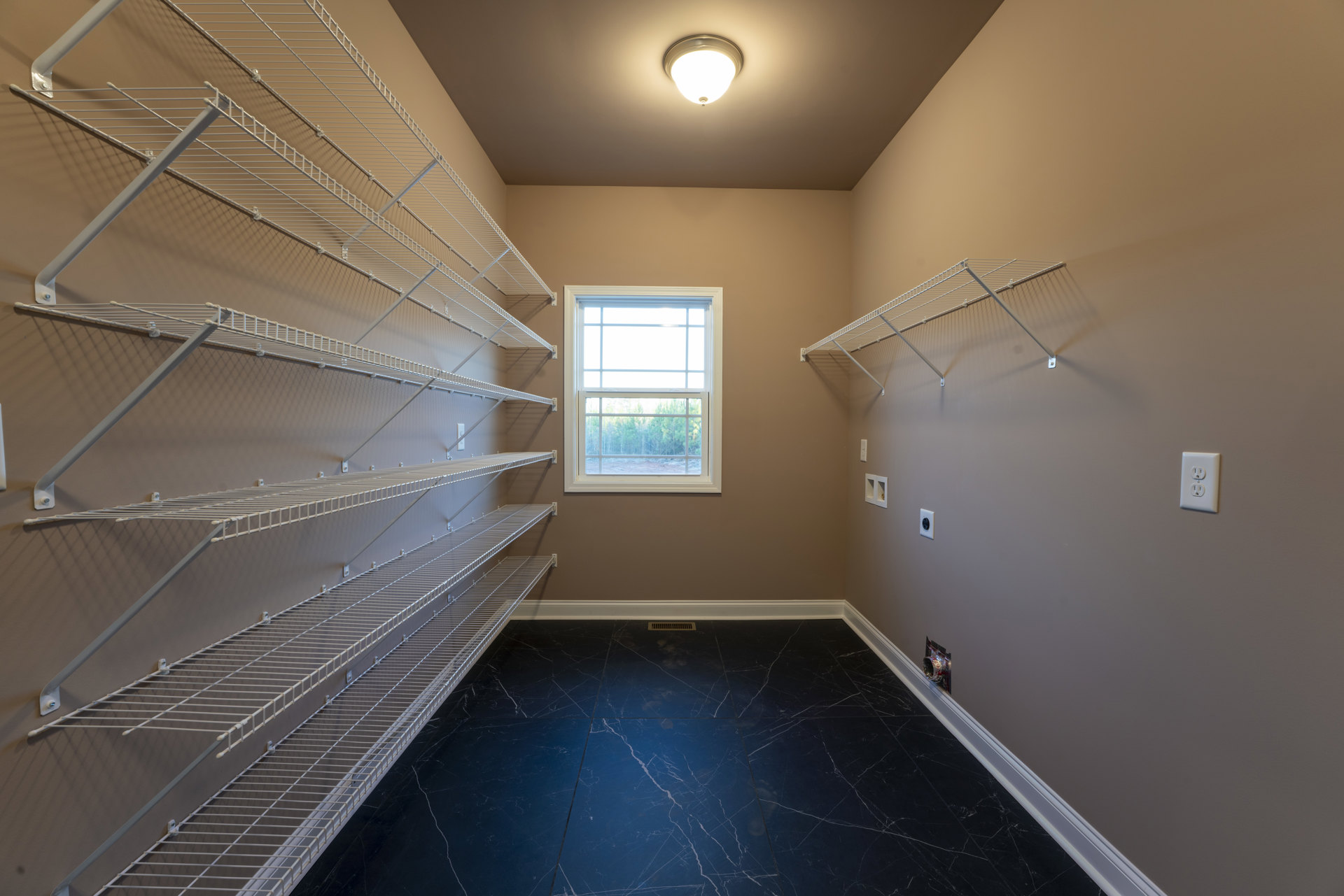 Built-in metal shelves on a plaster wall, large window with tree views, white electrical outlet, ceiling light fixture, hardwood floor in empty room
