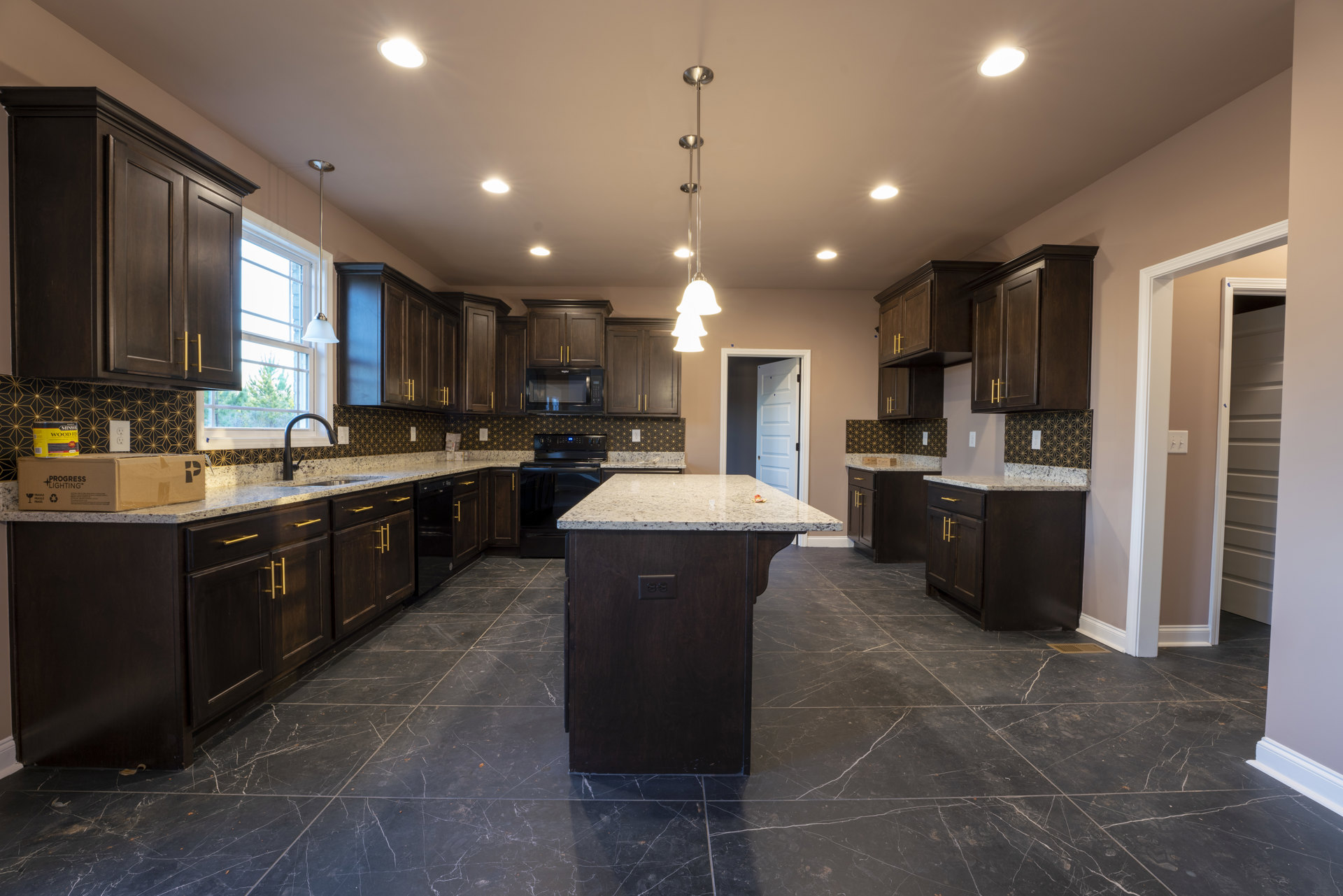 Kitchen with dark wood cabinets, granite countertops, central island with marble top, stainless steel light fixture, tiled floor, white door with black frame, and ceiling lighting
