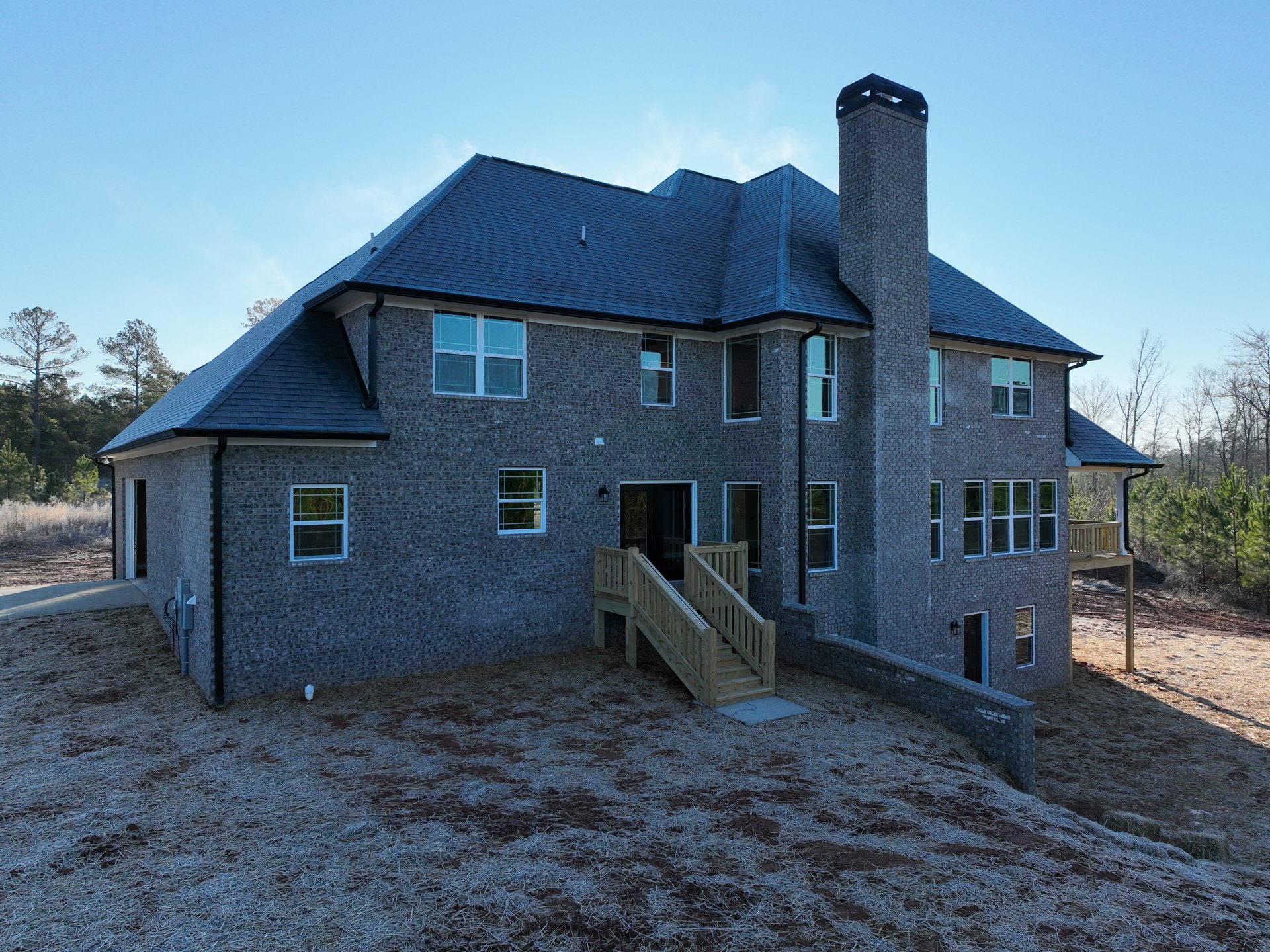 Two-story brick house with white-framed windows, wooden staircase leading to front entrance, surrounded by trees and greenery