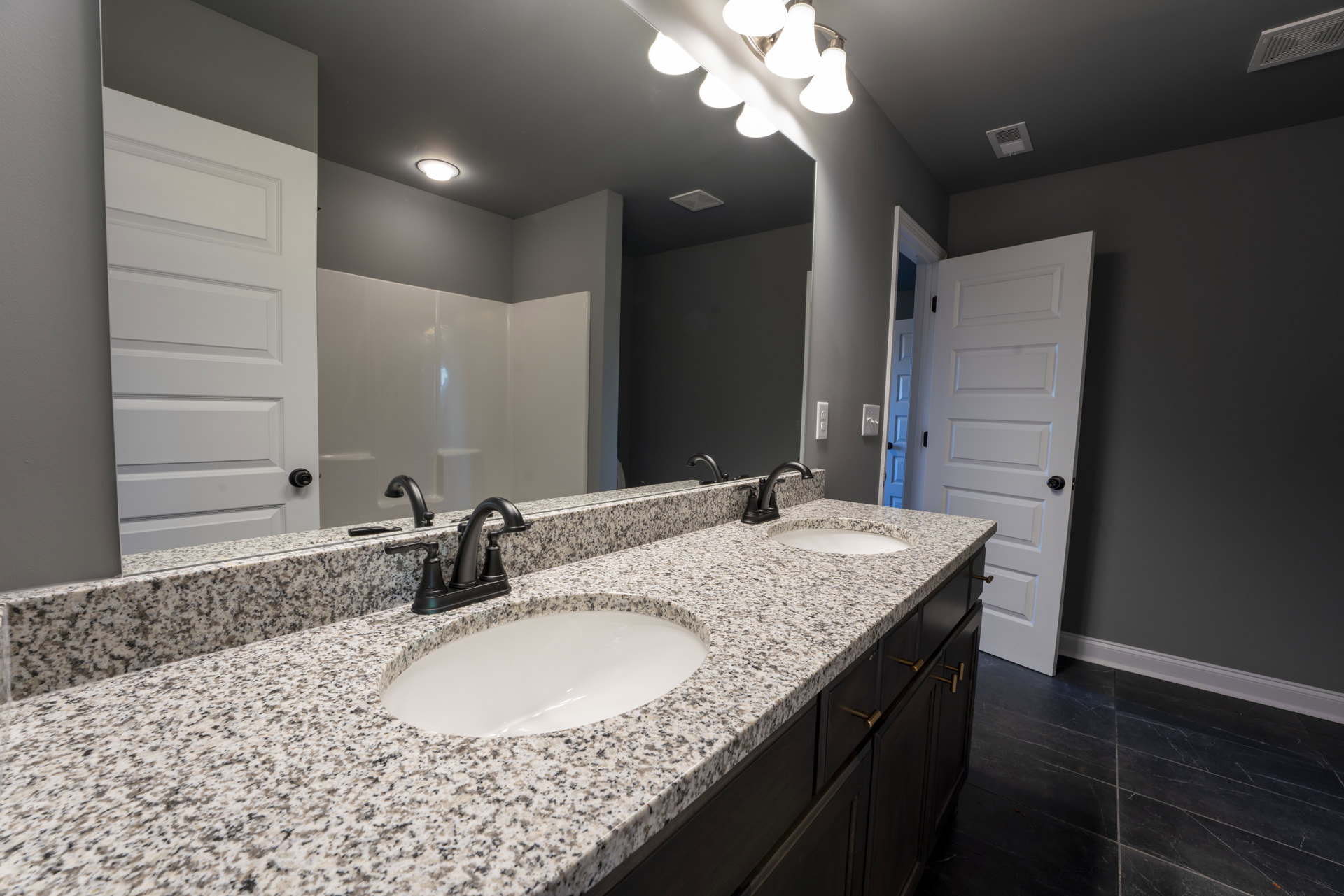 Marble countertop with white sink featuring black border, chrome faucet, white door with rectangular panels, ceiling vent, light-colored tile walls