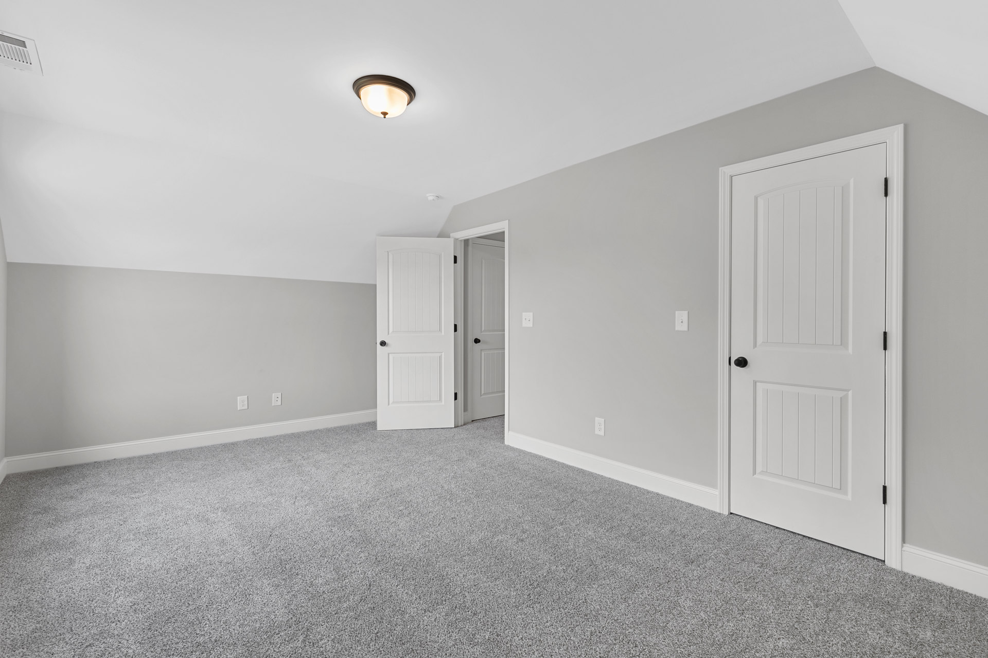 Carpeted room with white walls, two white doors featuring black knobs, white baseboard trim, and a ceiling-mounted light fixture