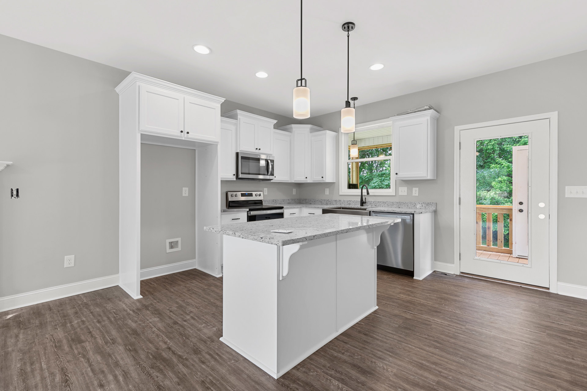 White kitchen with shaker cabinets, wood plank flooring, central island, stainless microwave, glass door leading to balcony, circular pendant light overhead