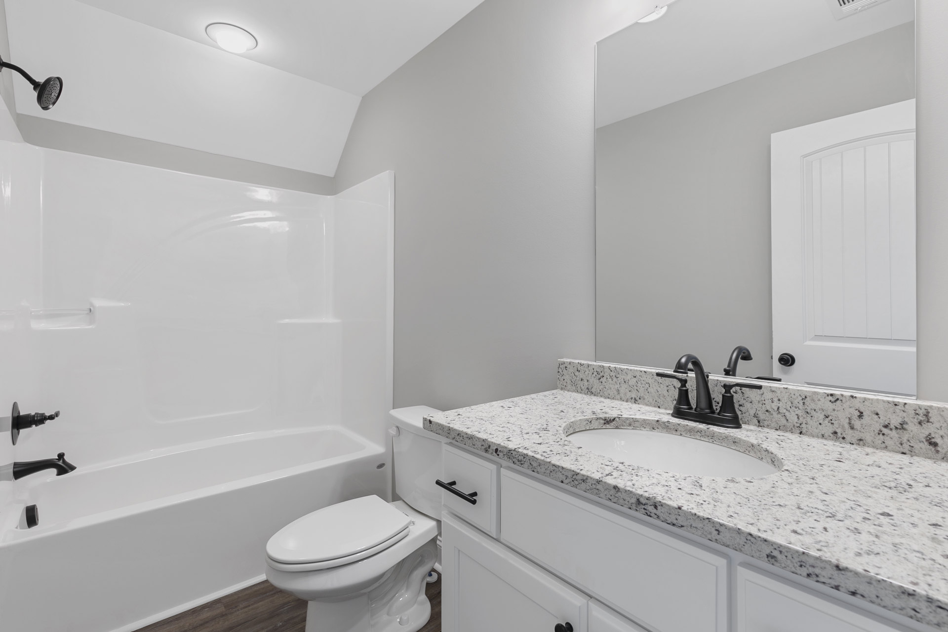 Modern bathroom featuring a freestanding white bathtub, white toilet with closed lid, rectangular sink set in a stone countertop, vertical paneled white door, black towel bar
